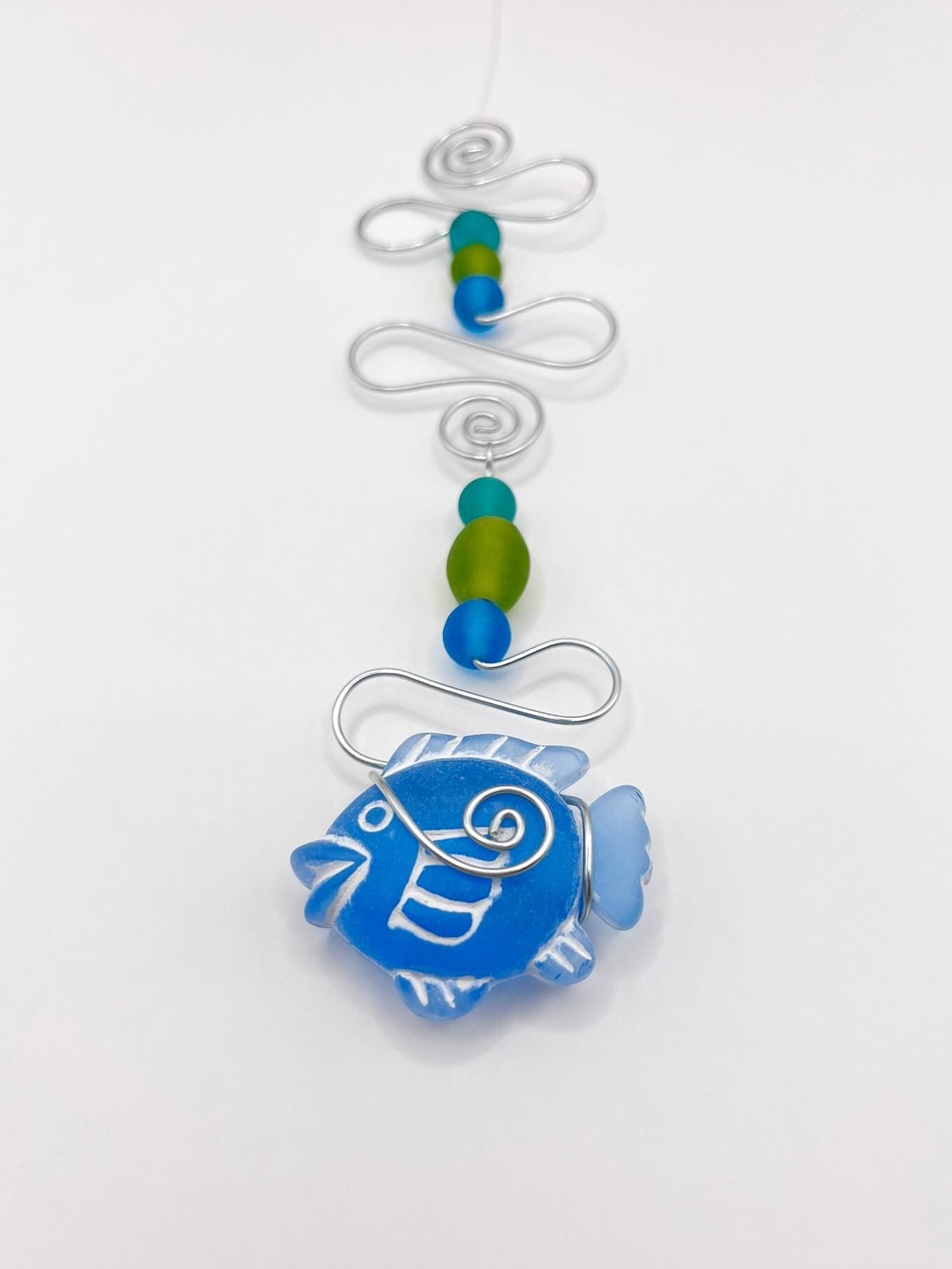 Decorative hanging ornament with blue fish, wire and colourful beads on a white background