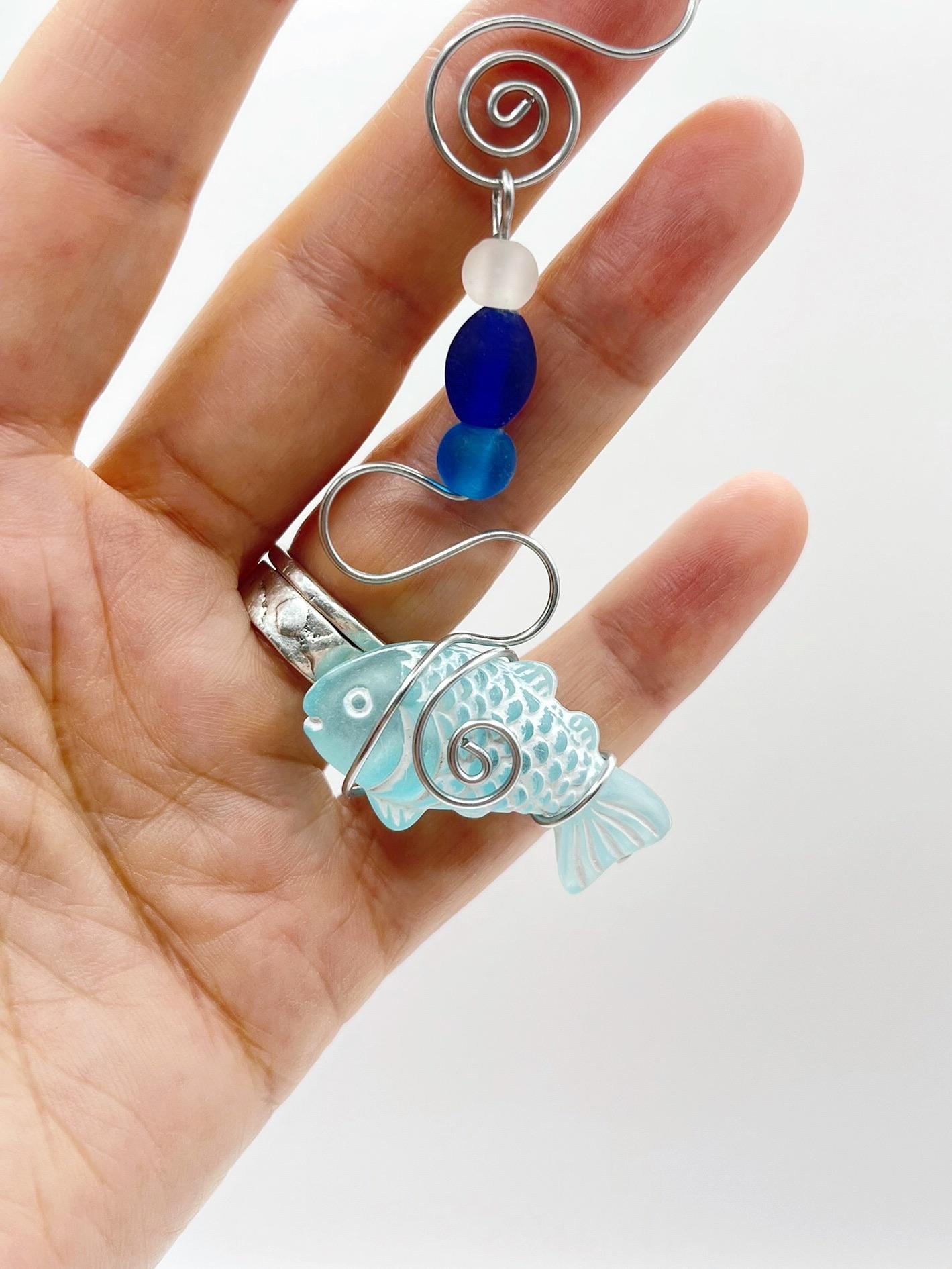 Decorative hanging fish ornament with wire and blue beads held in a hand against a white background