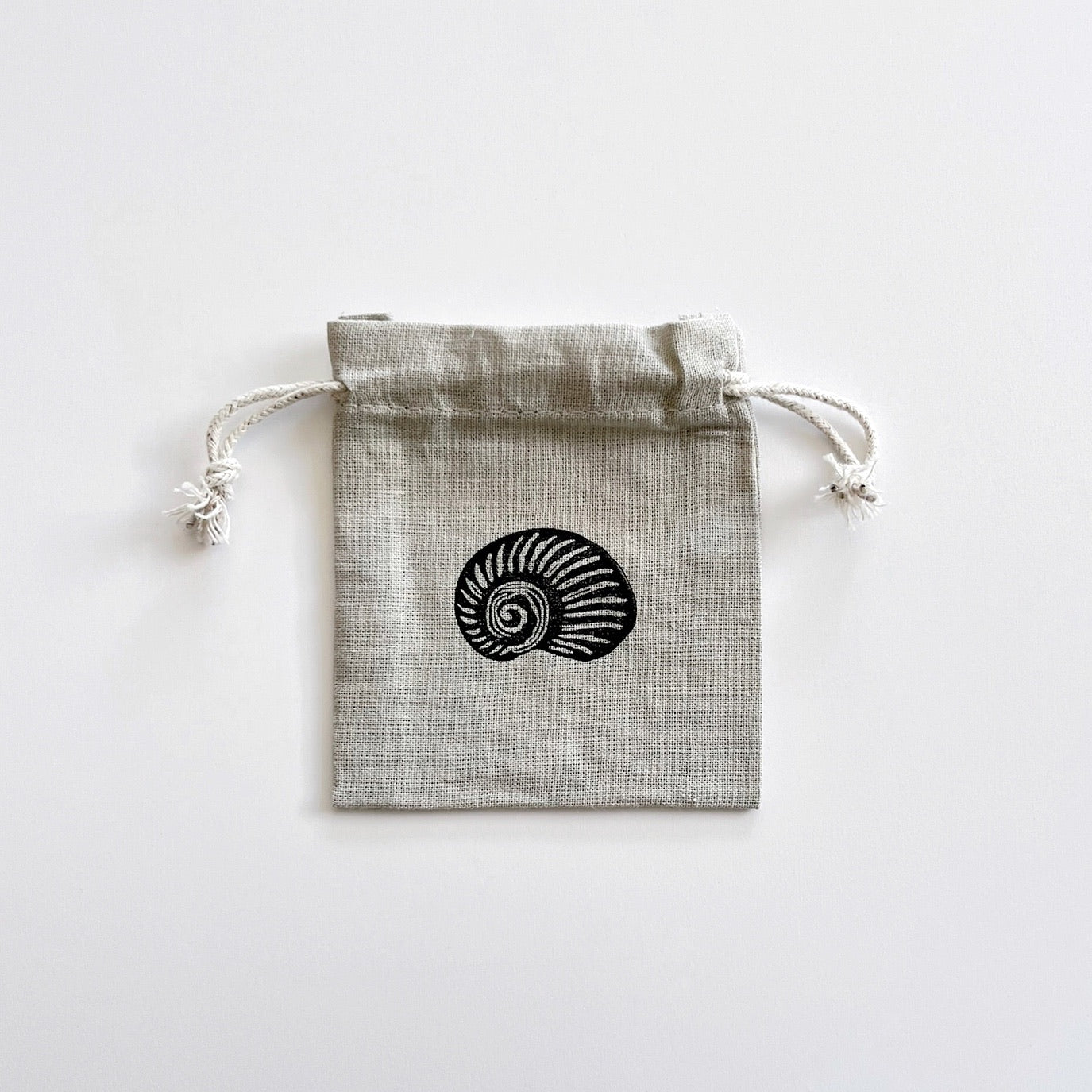 Grey drawstring cotton gift bags with a lino printed shell, laid flat on a white surface.