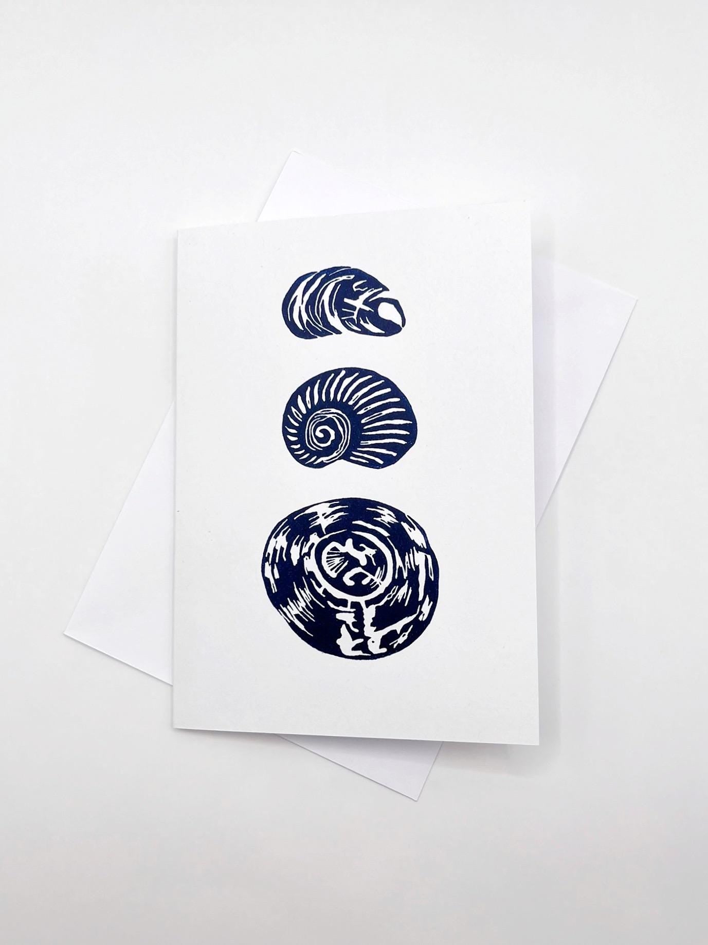 Three original lino cut blue shells on a white card with matching envelope, laid on a white background.