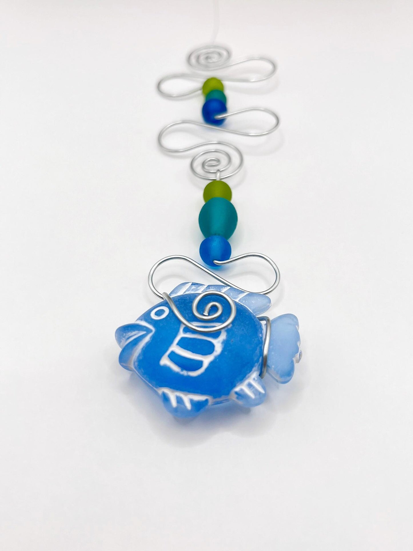 Decorative hanging ornament with blue fish, wire and colourful beads on a white background