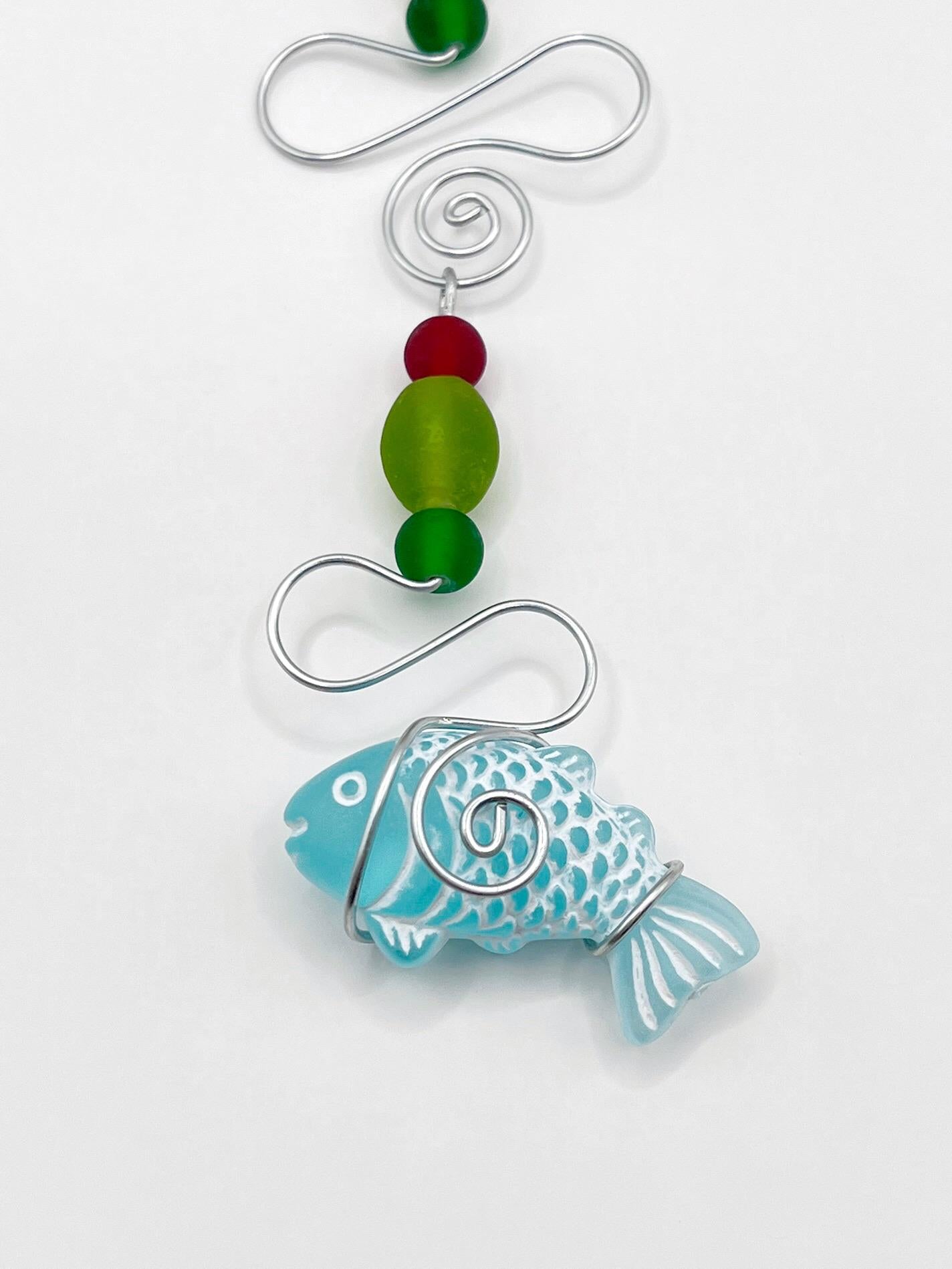 Close up of decorative hanging ornament with a fish design, wire and colourful beads on a white background