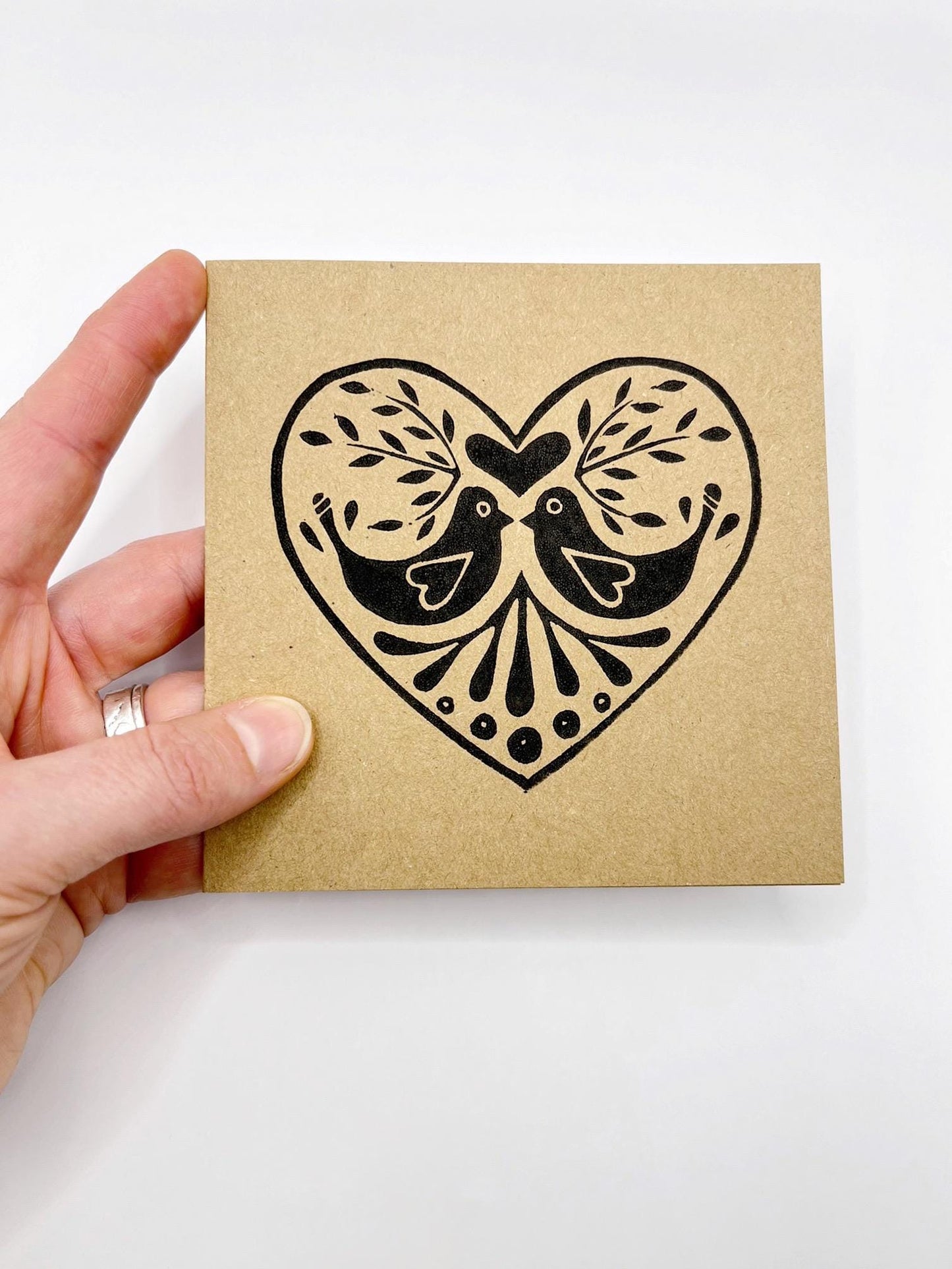 Hand holding a kraft card with a black heart design featuring two birds.