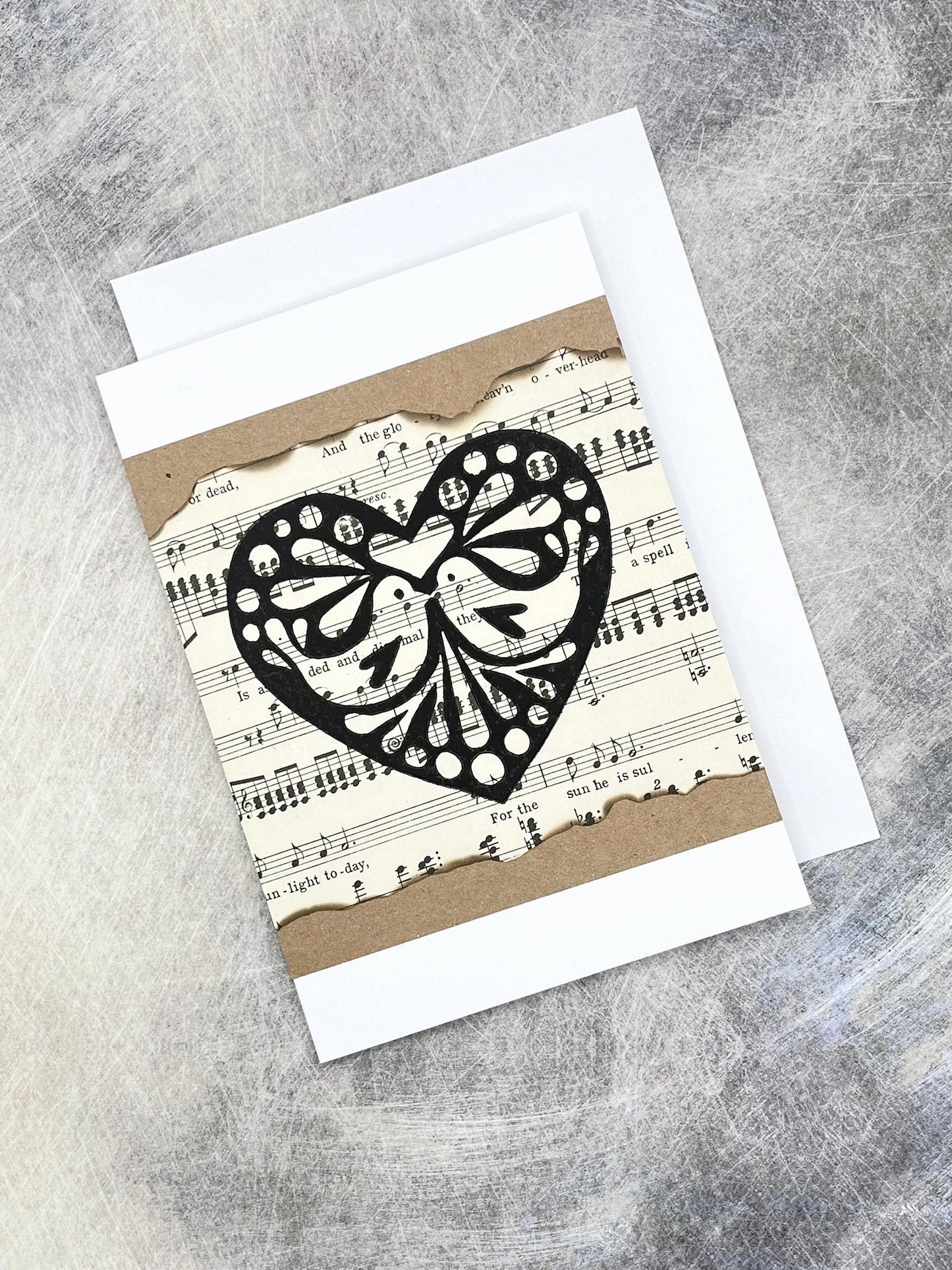Greeting card with an original lino printed black heart design on music sheet, laid on a textured background.
