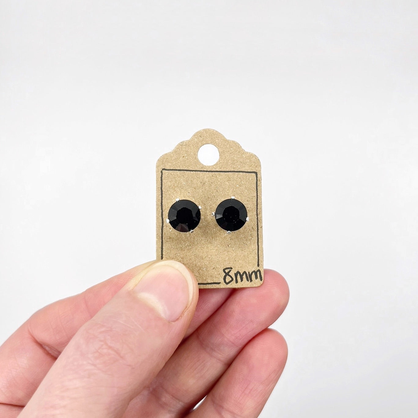 Black cut glass earrings on a small cardboard tag held by a hand against a white background