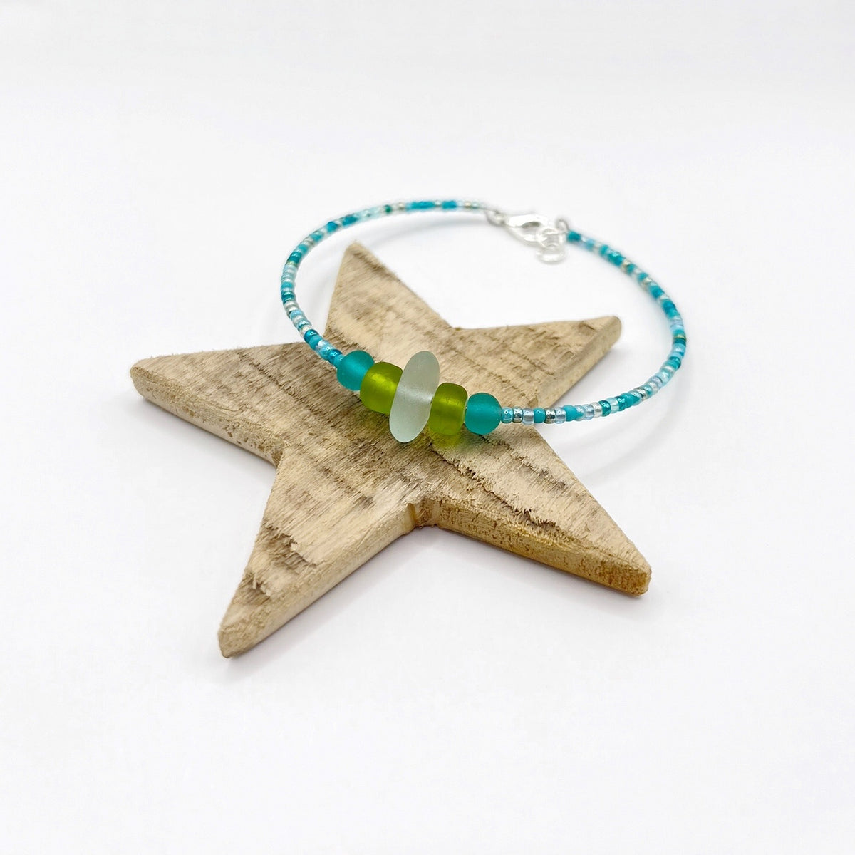 A turquoise beaded bracelet with lime and sea green frosted glass beads and a piece of sea foam coloured Cornish sea glass, finished with a silver plated lobster clasp and laid on a wooden star.