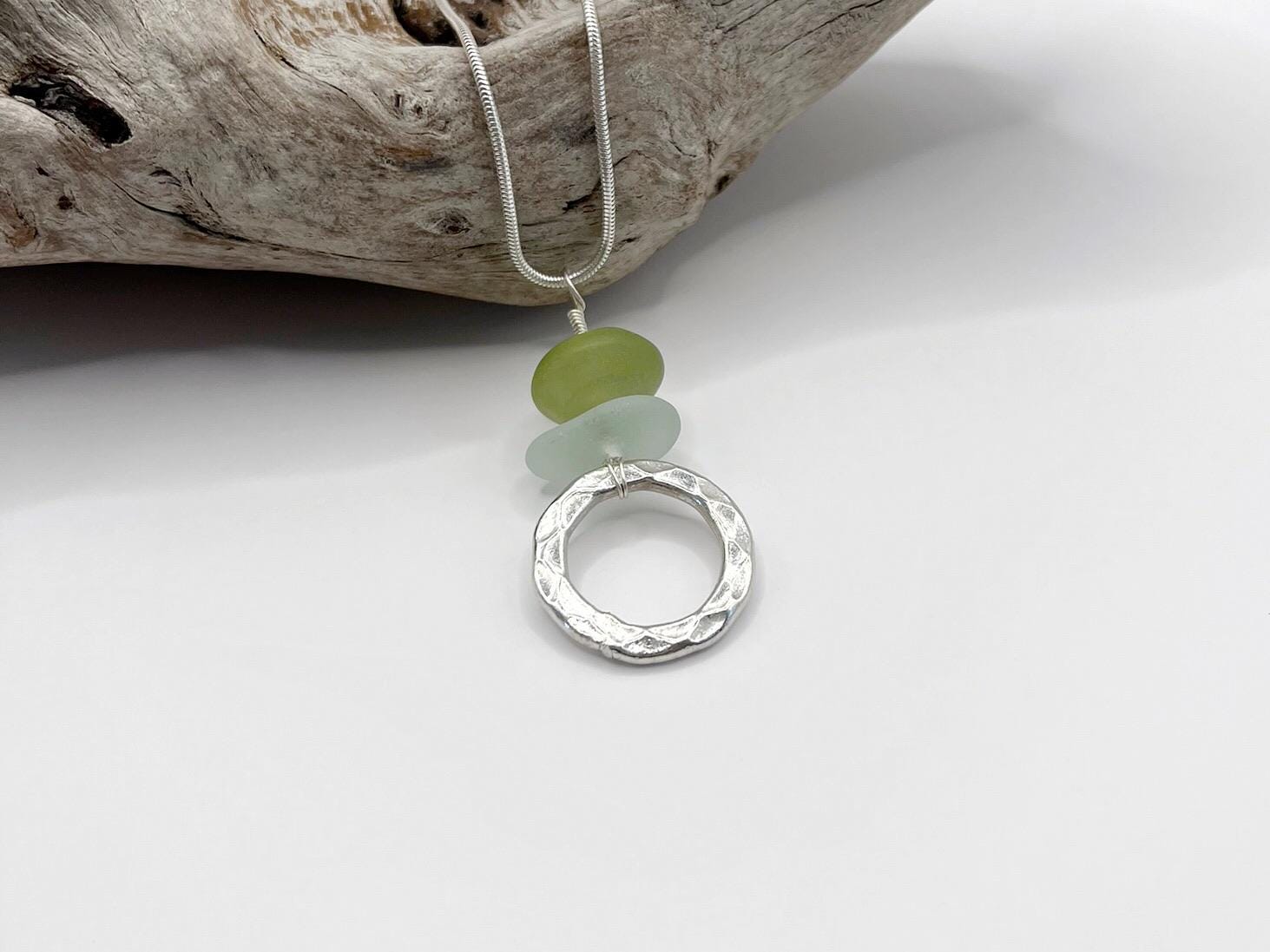 Necklace with a silver ring, green jade  bead and sea glass on a white surface with driftwood.