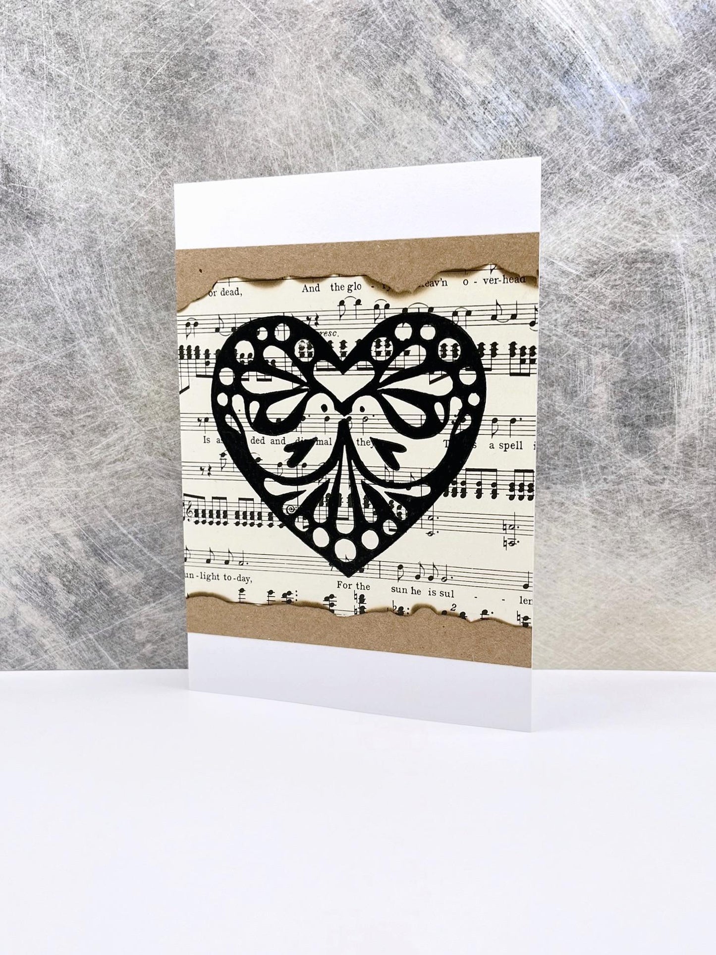 Card with original lino printed black heart design on music sheet stood against a textured background.