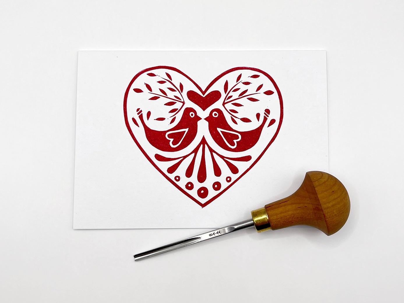 Decorative heart card with two birds laid on a white background. Photo includes lino cutting tool.