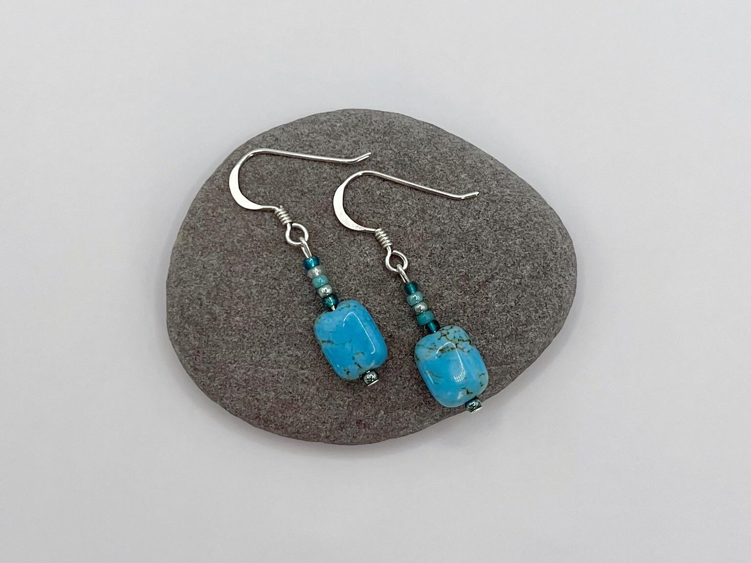 Pair of turquoise beaded earrings laid on a grey pebble