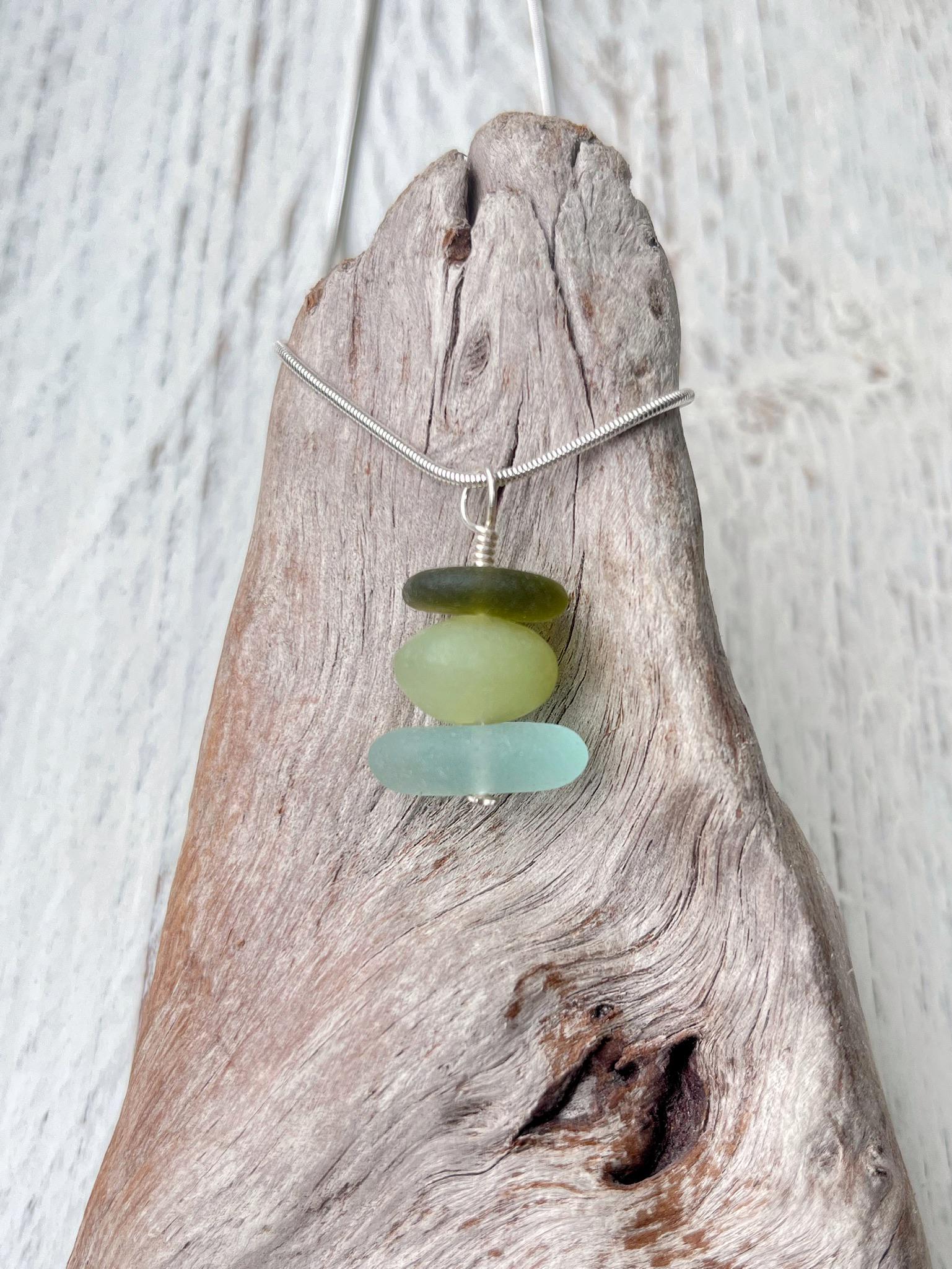 Necklace with green sea glass and a Jade bead sat against driftwood on a textured surface.