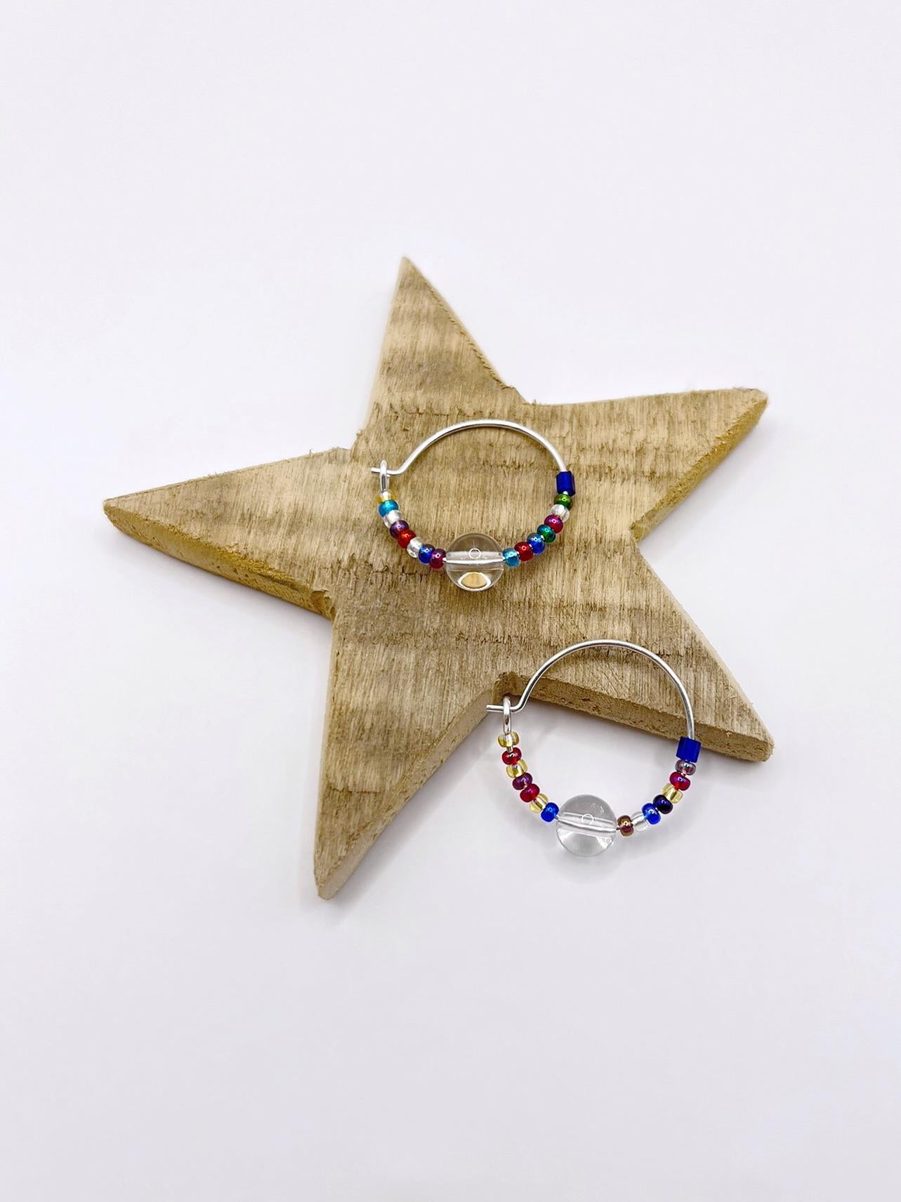 Rainbow seed bead and crystal hoop earrings laid on a wooden star against a white background.