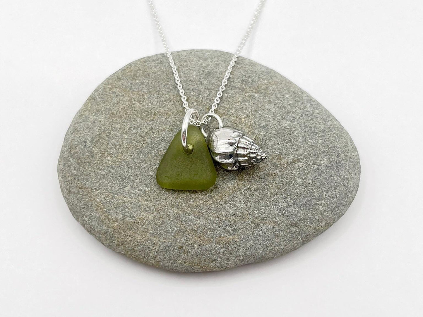 Necklace with a green sea glass and silver shell charm laid on a grey pebble.