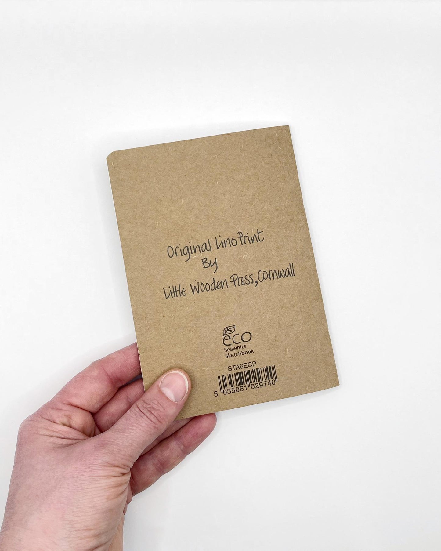 Hand holding a brown kraft notebook showing the back with 'Original Print' text against a white background
