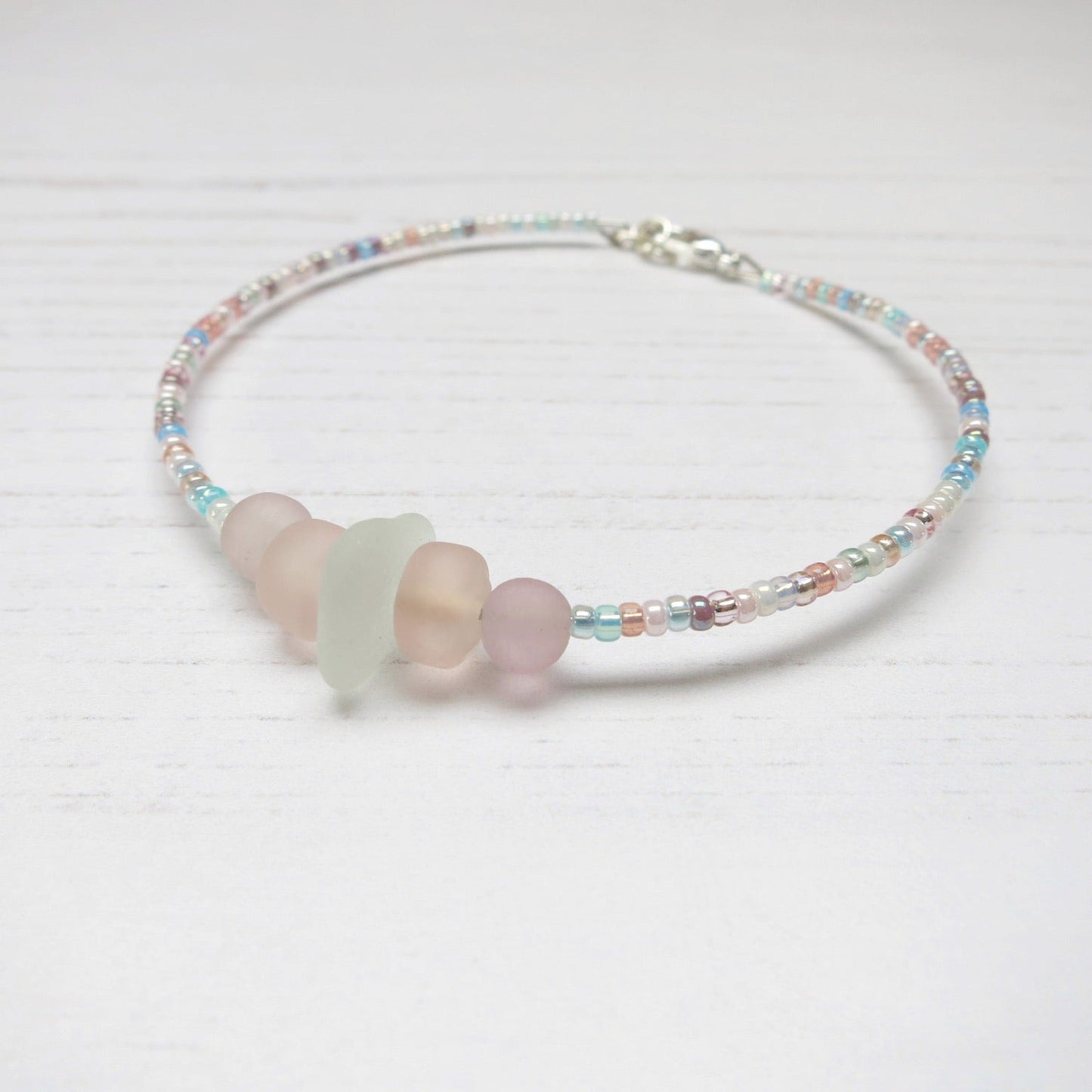 Bracelet with white sea glass and pastel beads laid on a white background