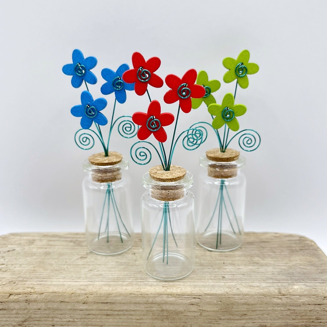 Three little glass bottles with wooden flowers sat on driftwood
