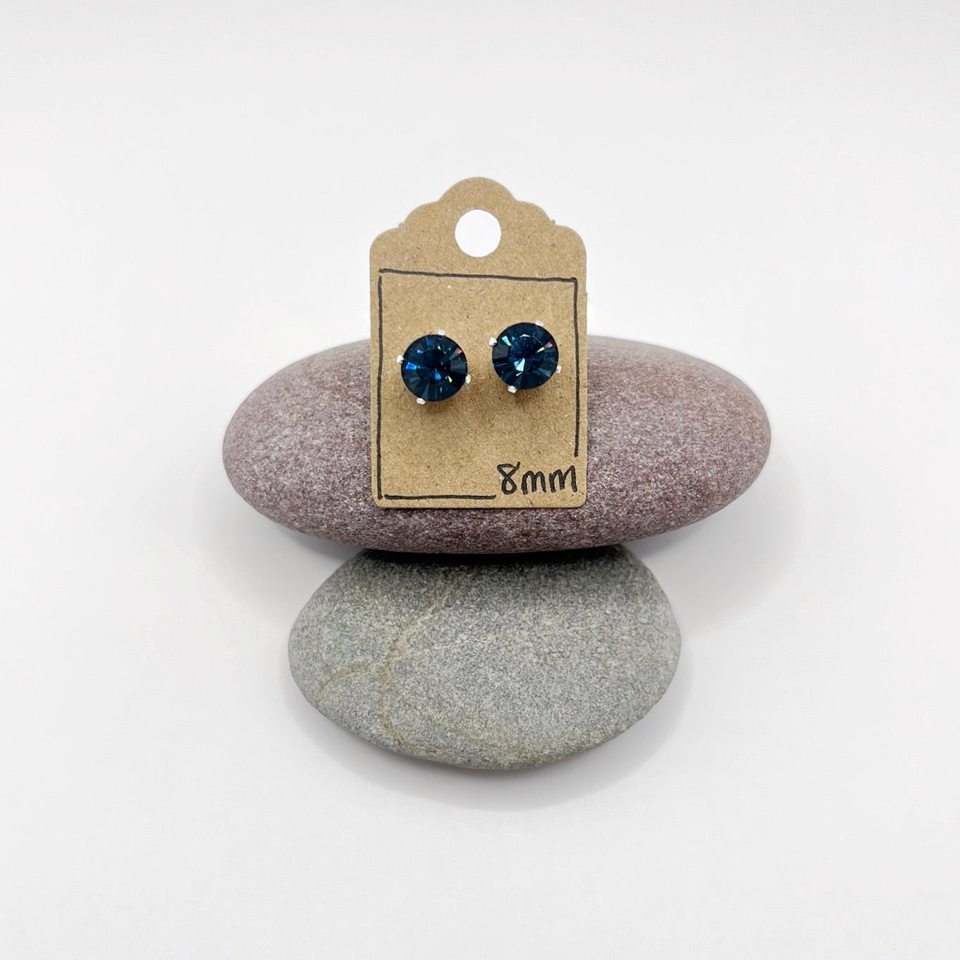 Pair of blue stud earrings on a cardboard backing card, placed on two stones.