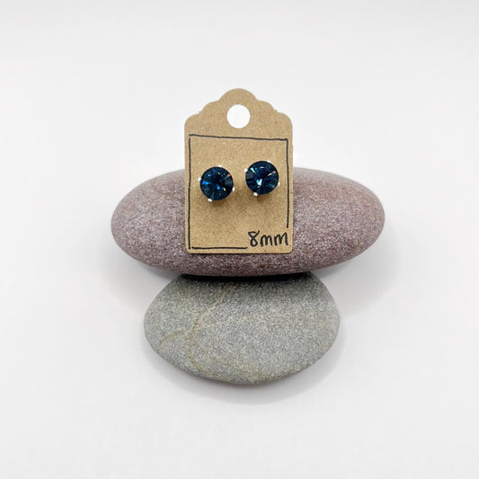 Pair of blue stud earrings on a cardboard backing card, placed on two stones.