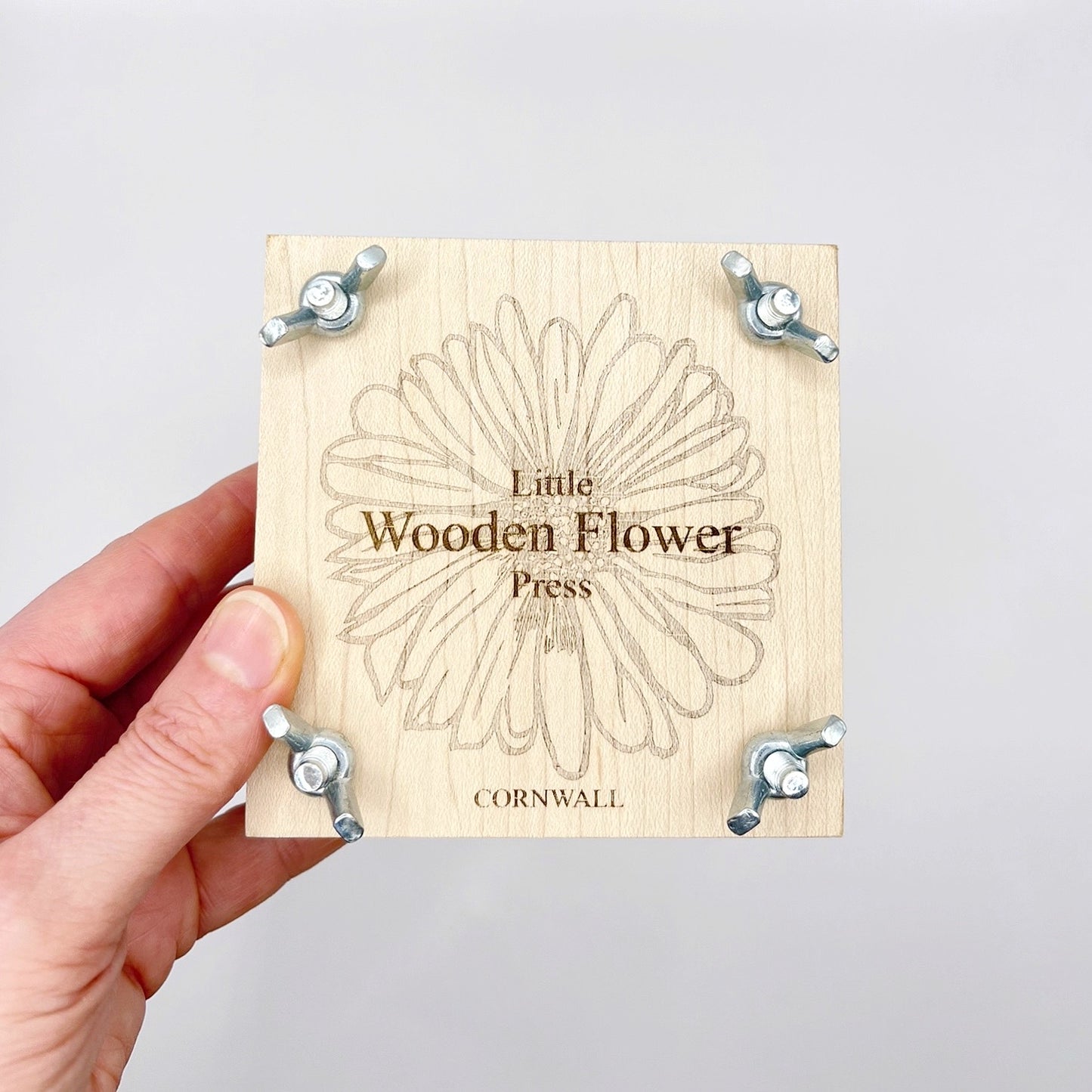 Wooden flower press with 'Little Wooden Flower Press' branding held by a hand against a white background