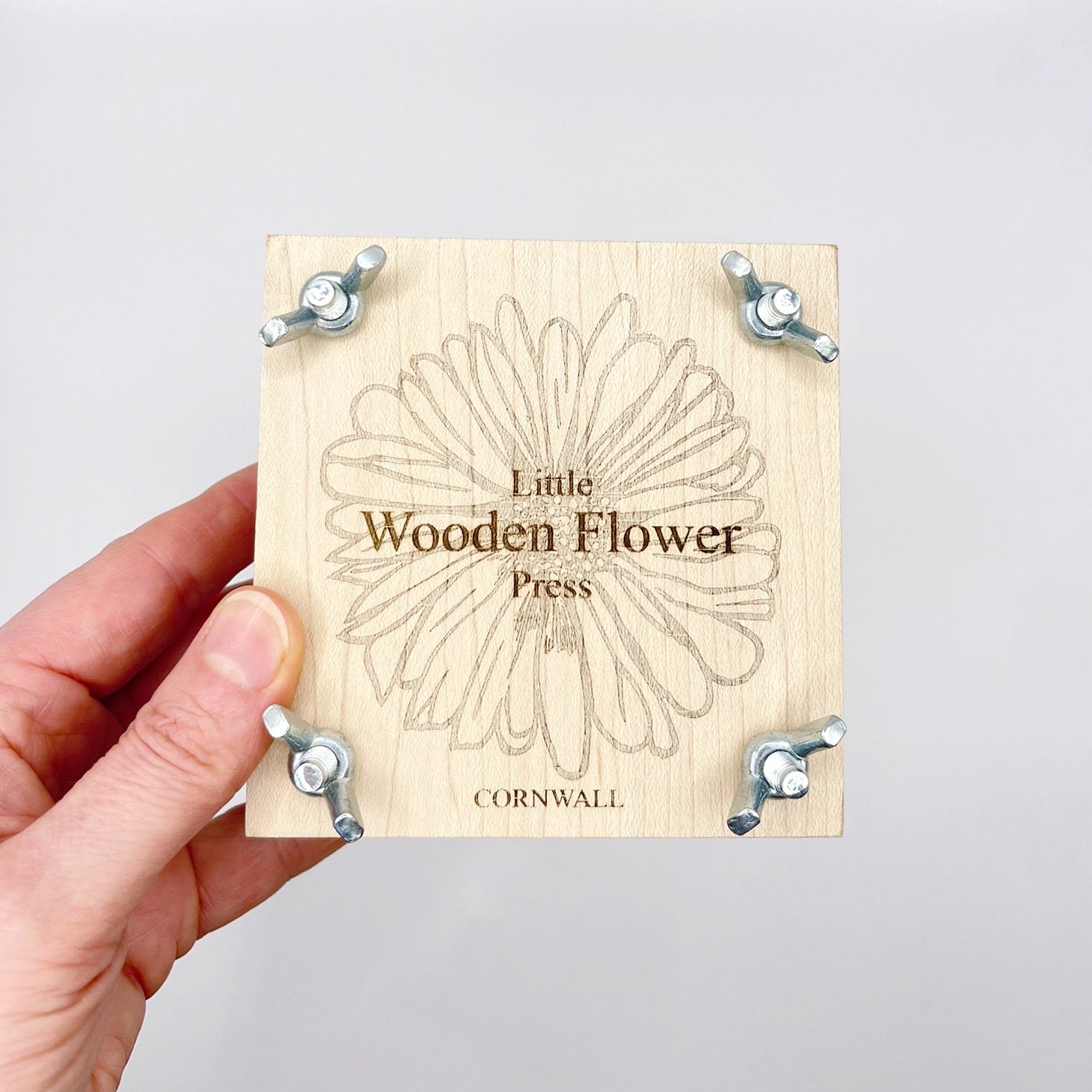 Wooden flower press with 'Little Wooden Flower Press' branding held by a hand against a white background