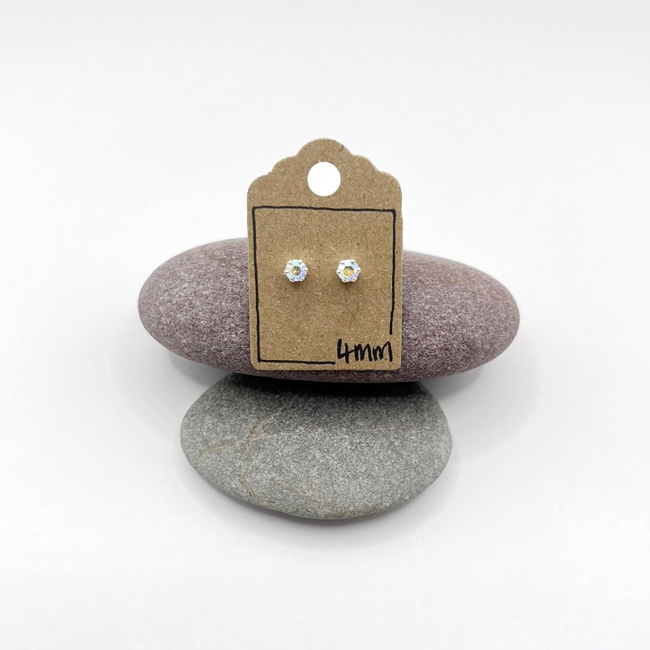 Pair of cut glass stud earrings on a cardboard backing with '4mm' text, placed on two stones.