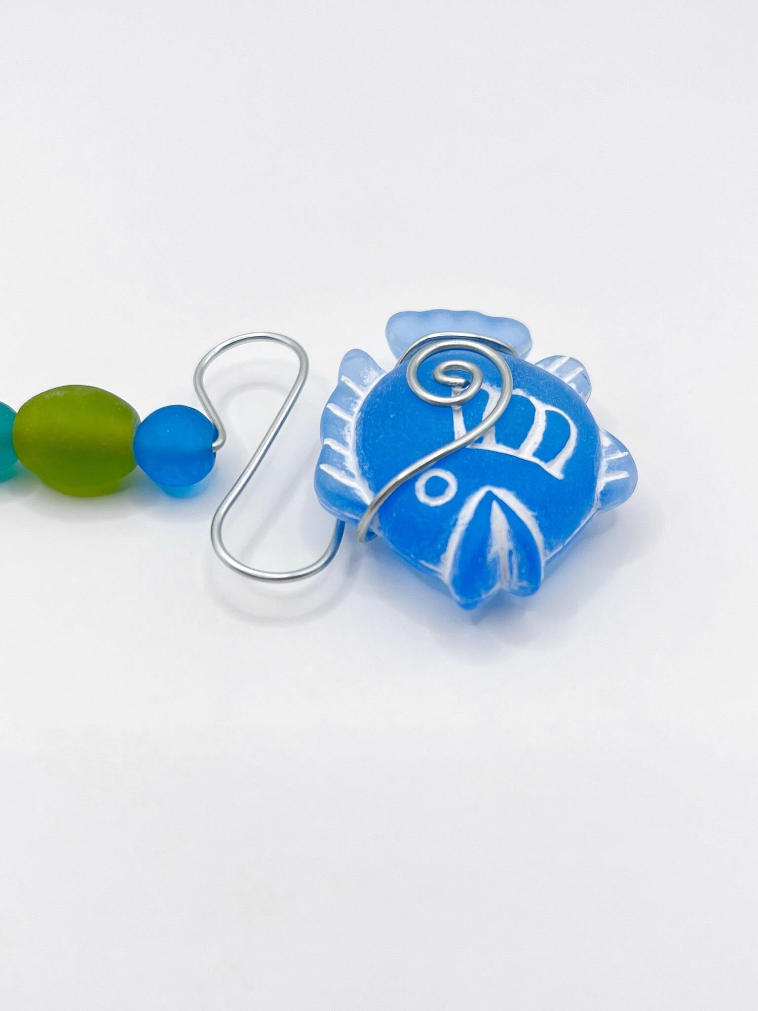 Close up of decorative hanging ornament with blue fish, wire and colourful beads on a white background