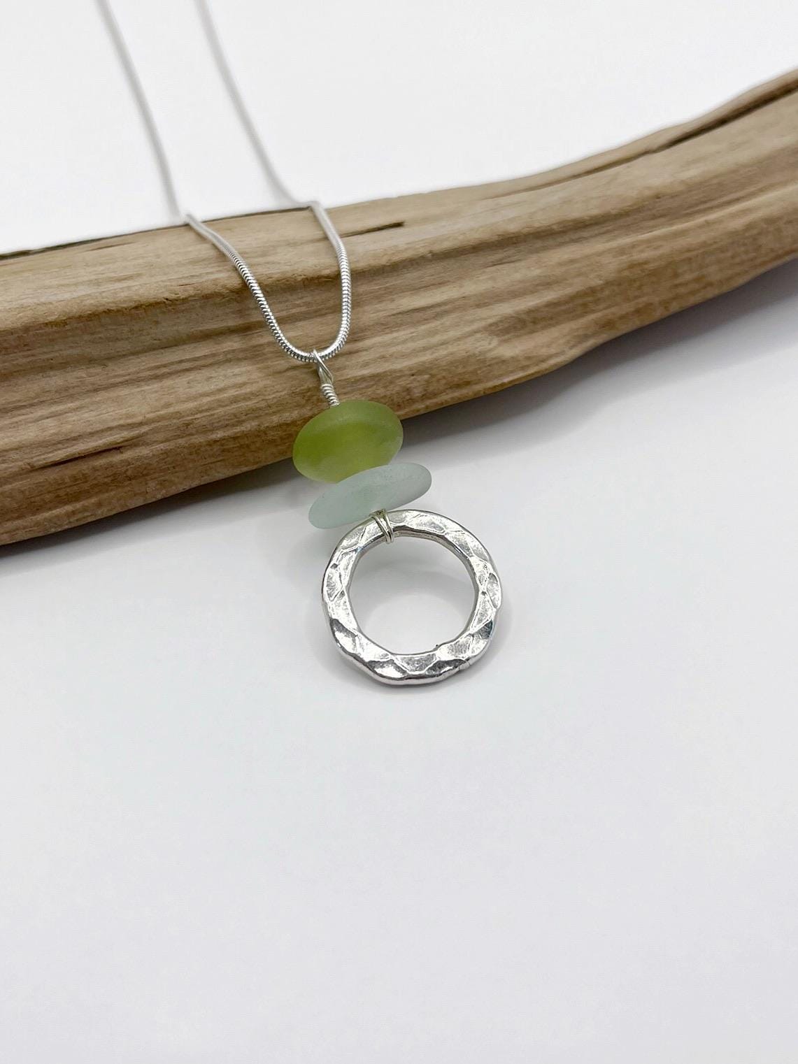 Necklace with a silver ring pendant, green jade bead and sea glass on a white background