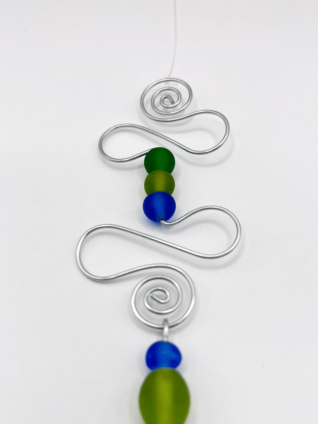Close up of decorative hanging with blue fish, wire and colourful beads on a white background