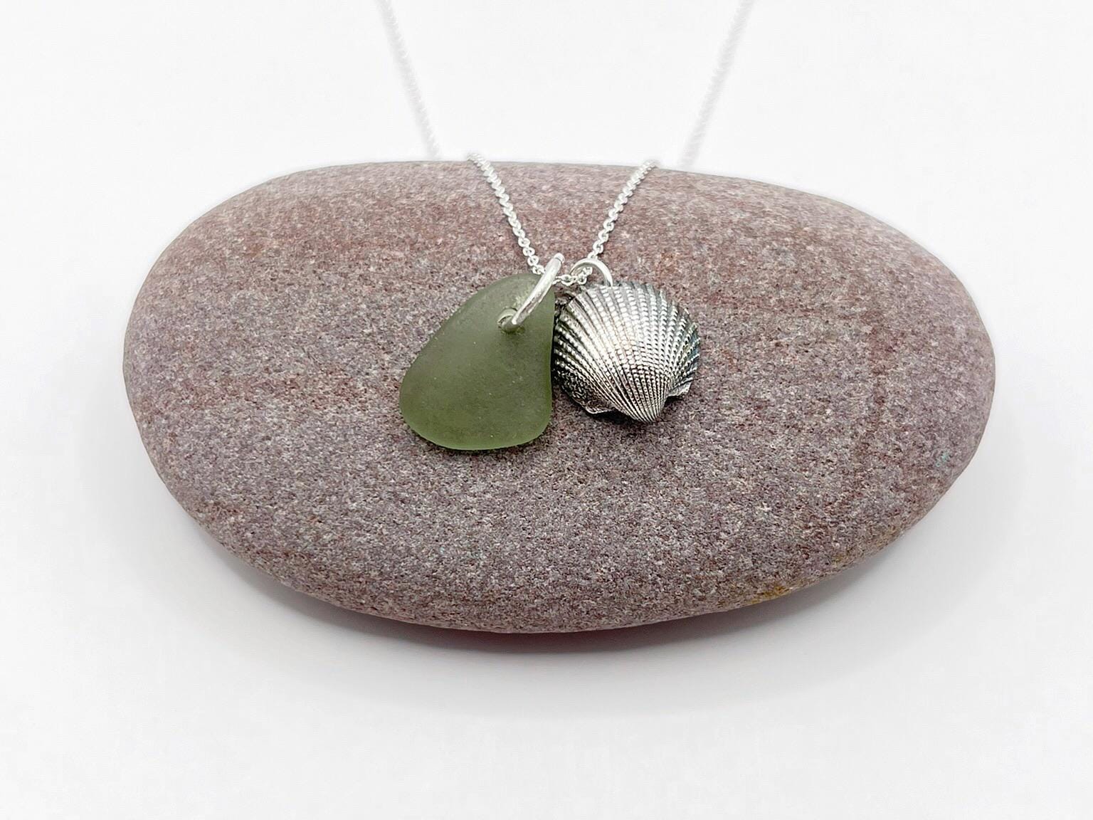 Necklace with green sea glass and a silver shell pendant laid on a purple pebble