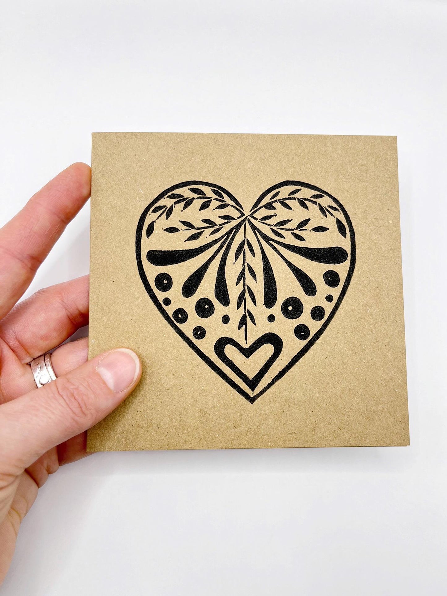 Card with an original lino printed black heart design on Kraft card held in a hand against a white background