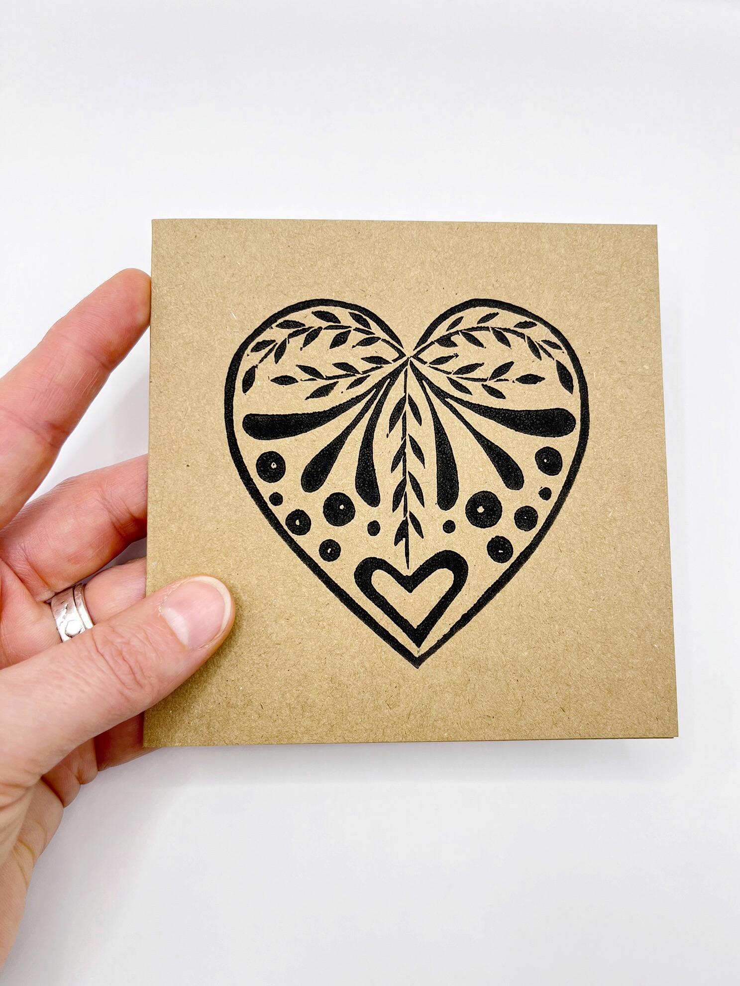 Card with an original lino printed black heart design on Kraft card held in a hand against a white background