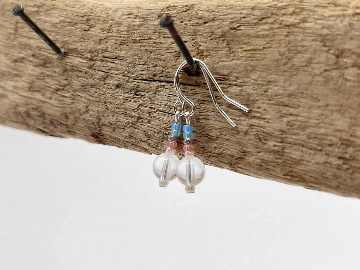 Silver earrings with crystal and pastel seed beads hanging on a piece of driftwood