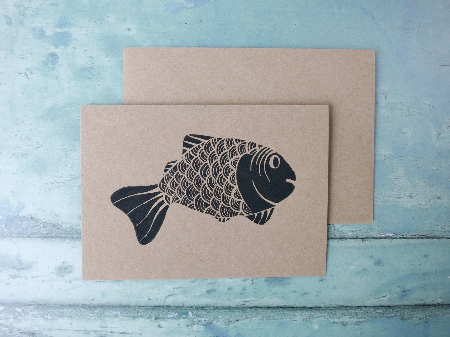 Kraft paper card with original lino printed fish laid on a textured surface. 