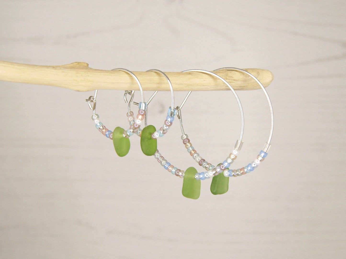 Hoop earrings with pastel seed beads and green sea glass hanging on driftwood