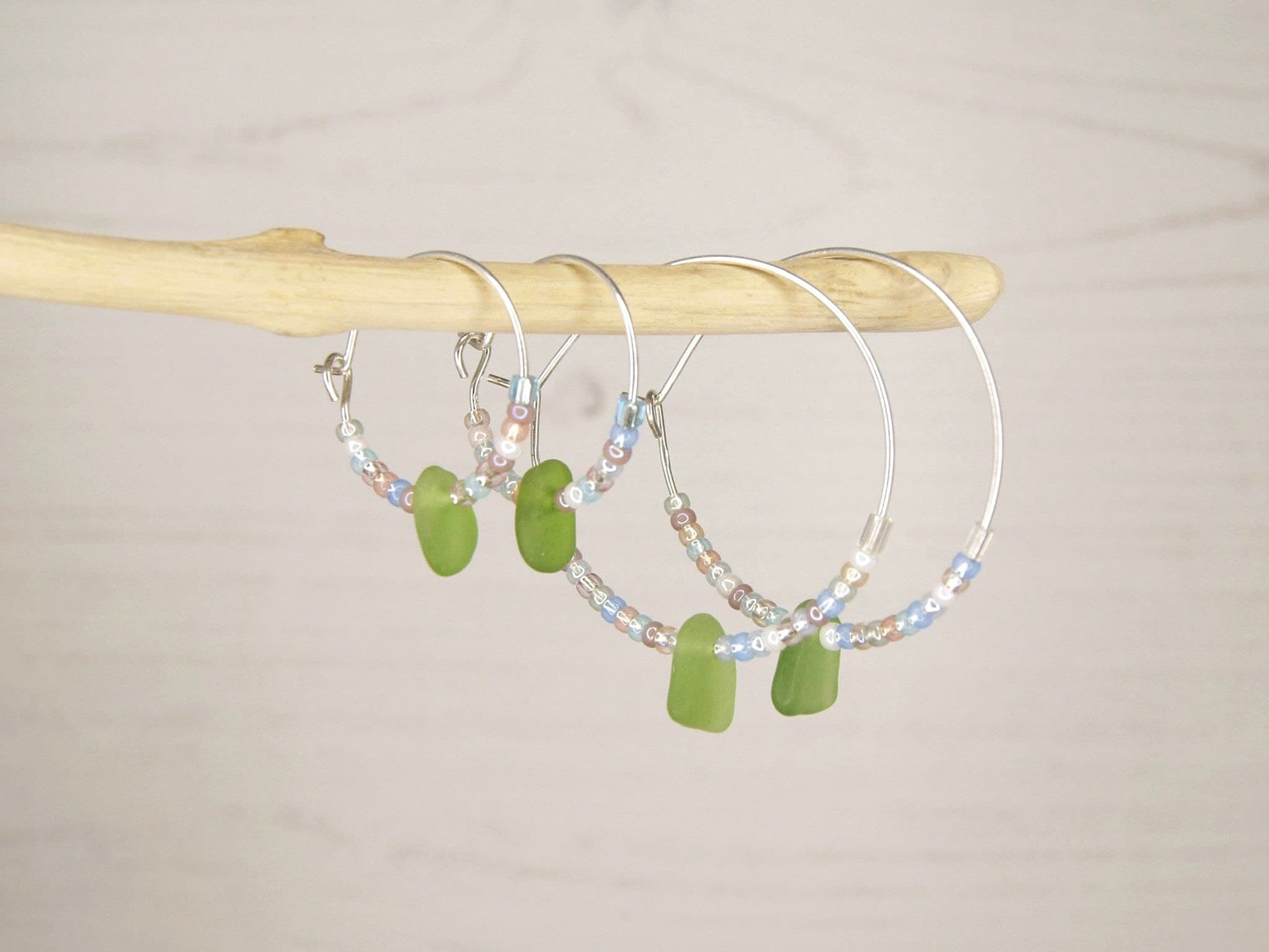 Hoop earrings with pastel seed beads and green sea glass hanging on driftwood