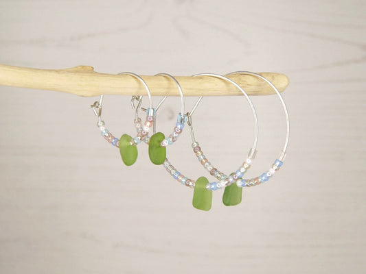 Hoop earrings with pastel seed beads and green sea glass hanging on driftwood