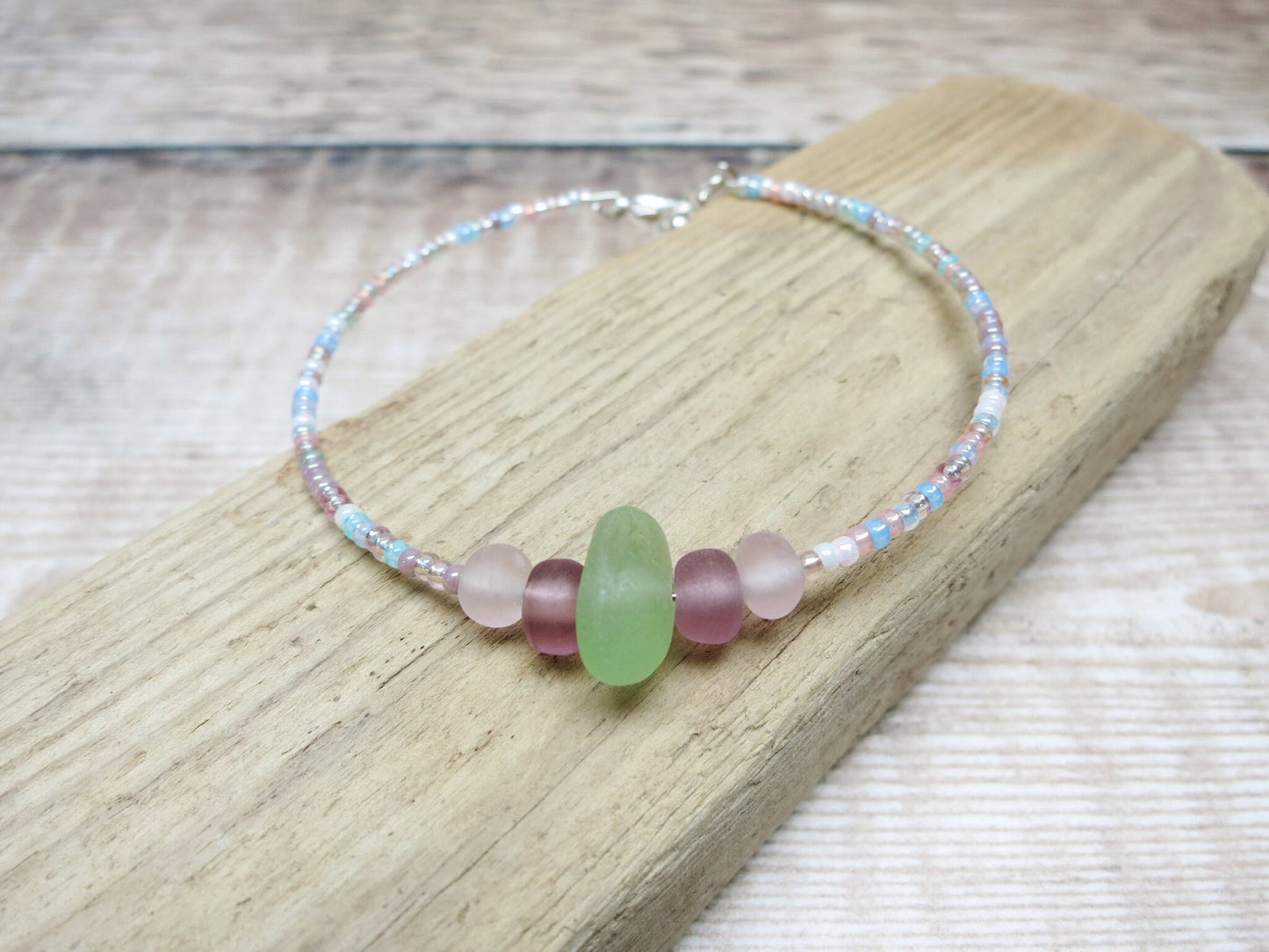 Pastel seed beaded bracelet with pale green sea glass laid on driftwood