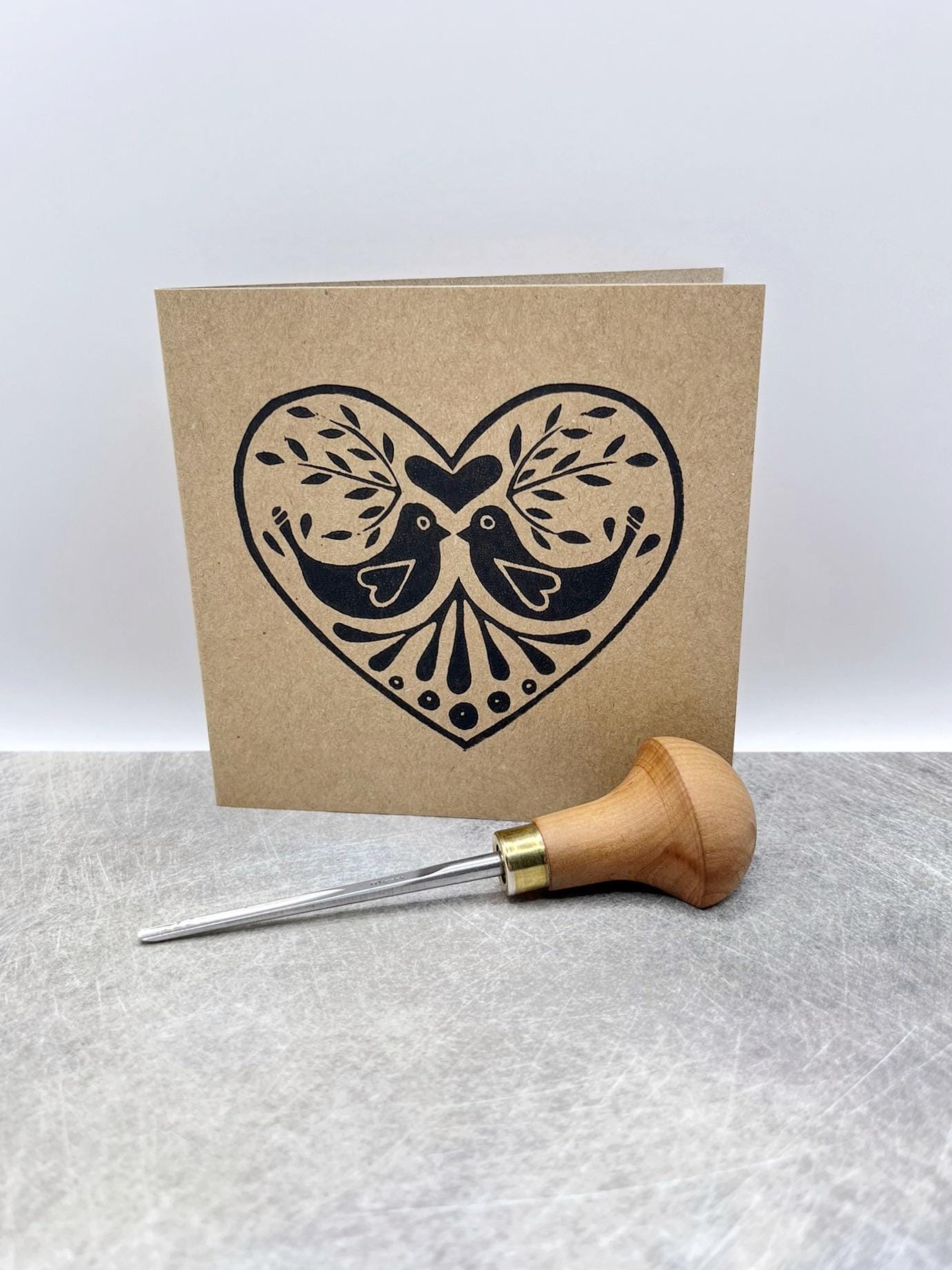 Kraft card with an original lino printed heart featuring two birds. Included in the photo is the lino cutting tool used.