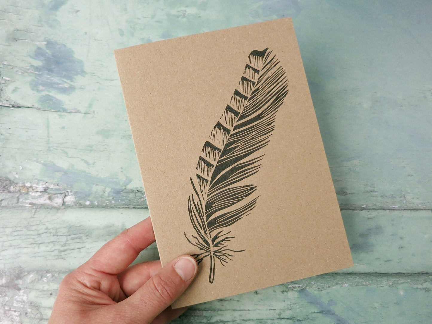 Hand holding a brown card with a black feather design on a textured blue surface