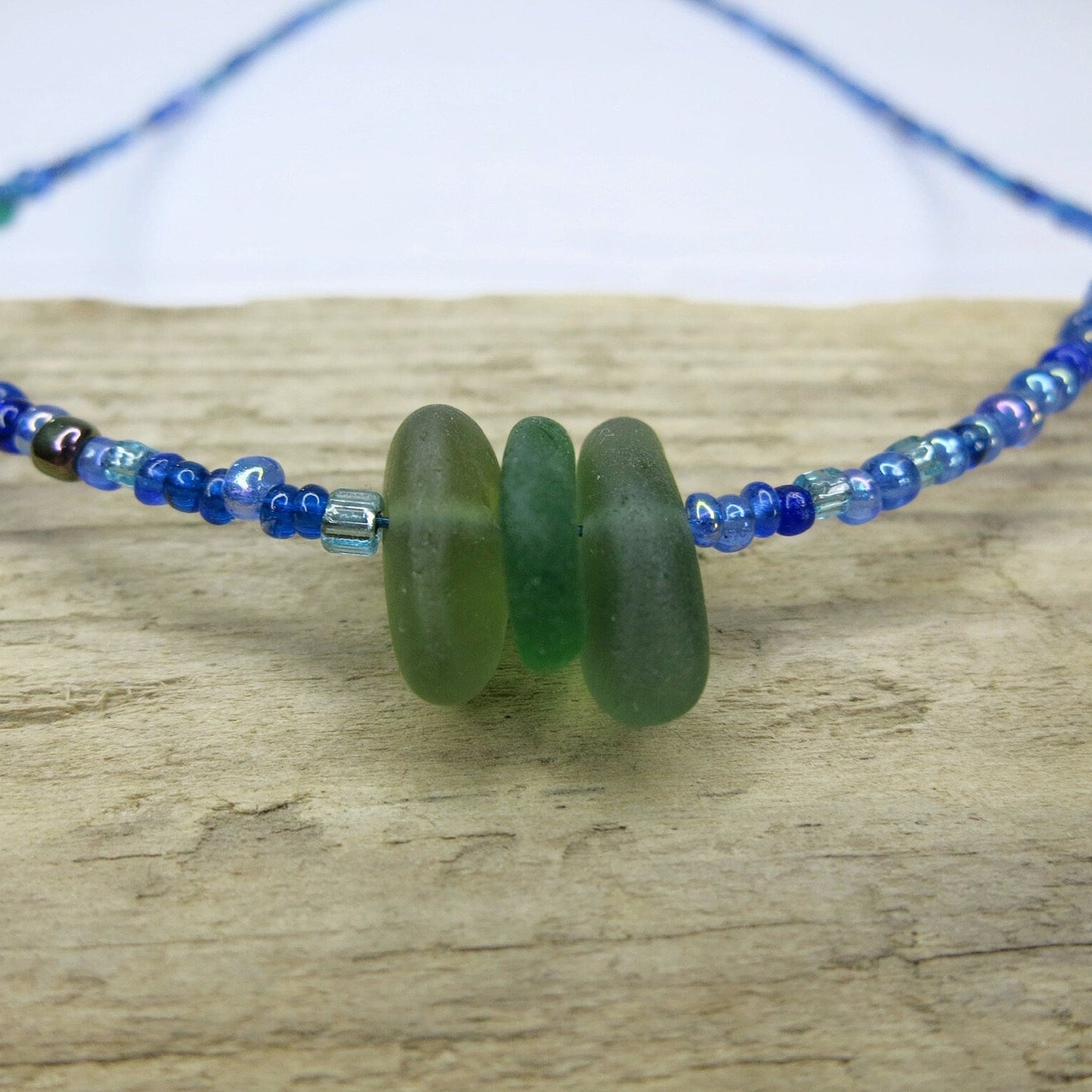 Close up of blue seed bead necklace with green sea glass laid on driftwood.