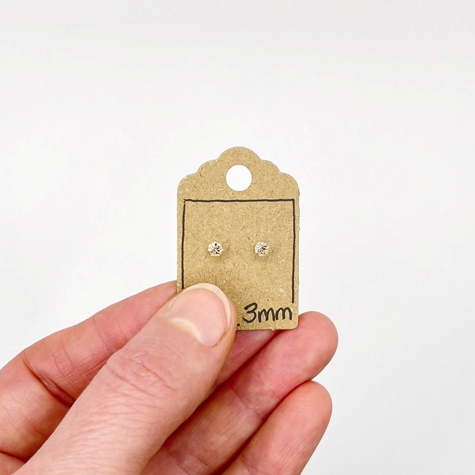 Hand holding a small cardboard earring card with two silver earrings on a white background
