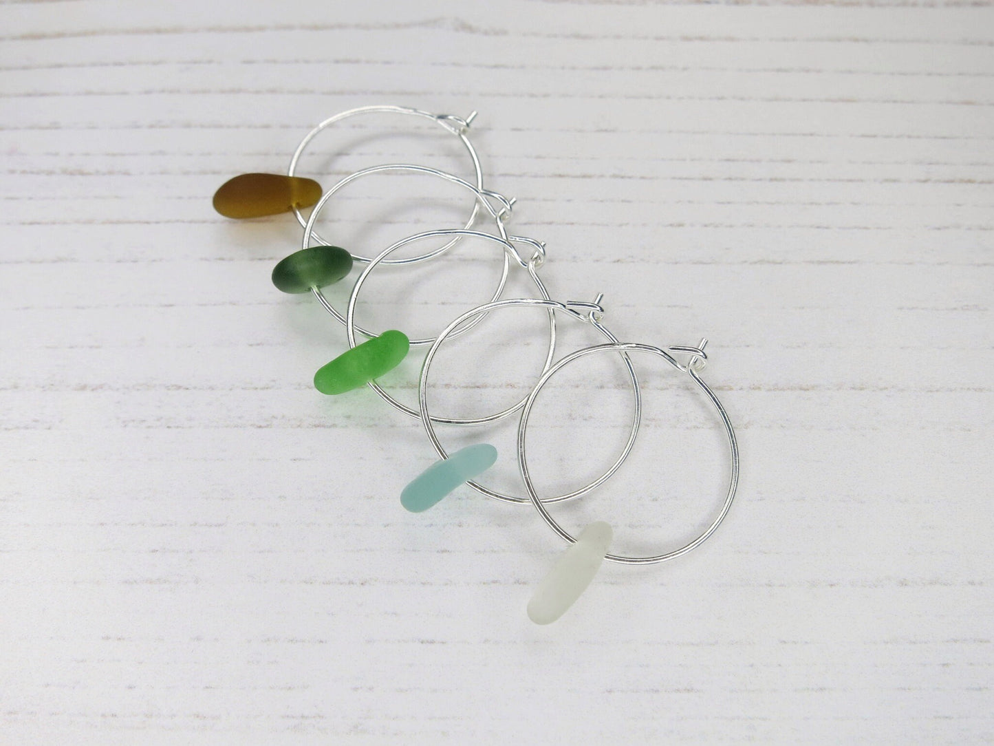 Silver hoop earrings with colourful sea glass laid on a white background