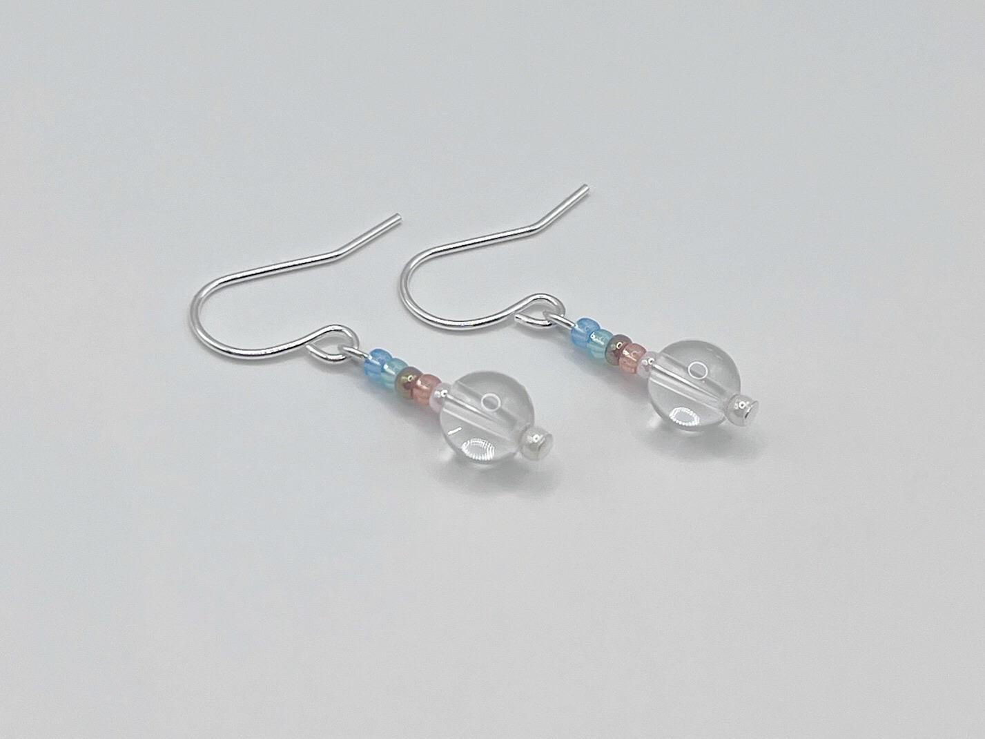 Silver earrings with clear crystal and pastel seed  beads laid on a white background