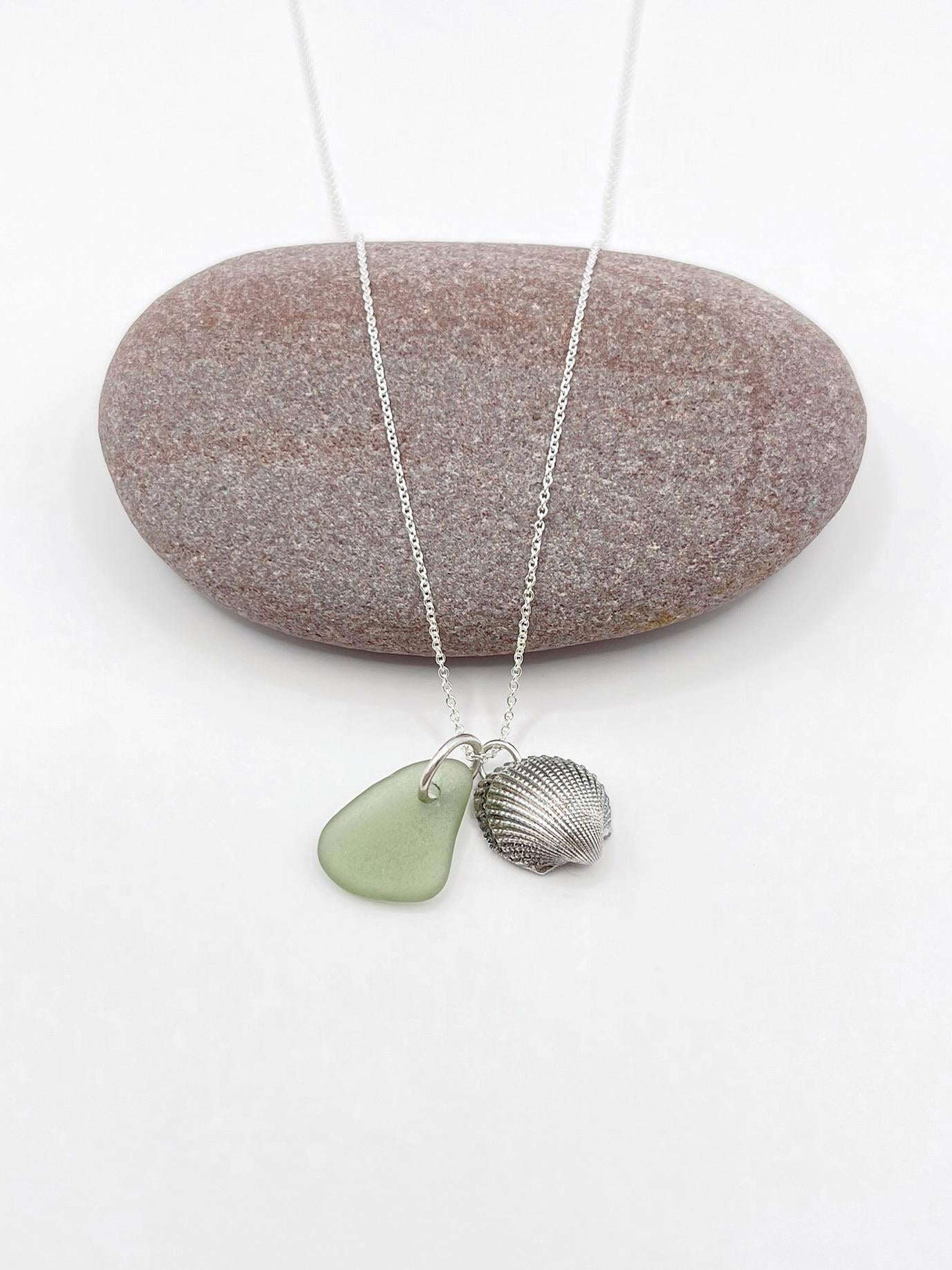 Necklace with green sea glass and a silver shell laid on a purple pebble