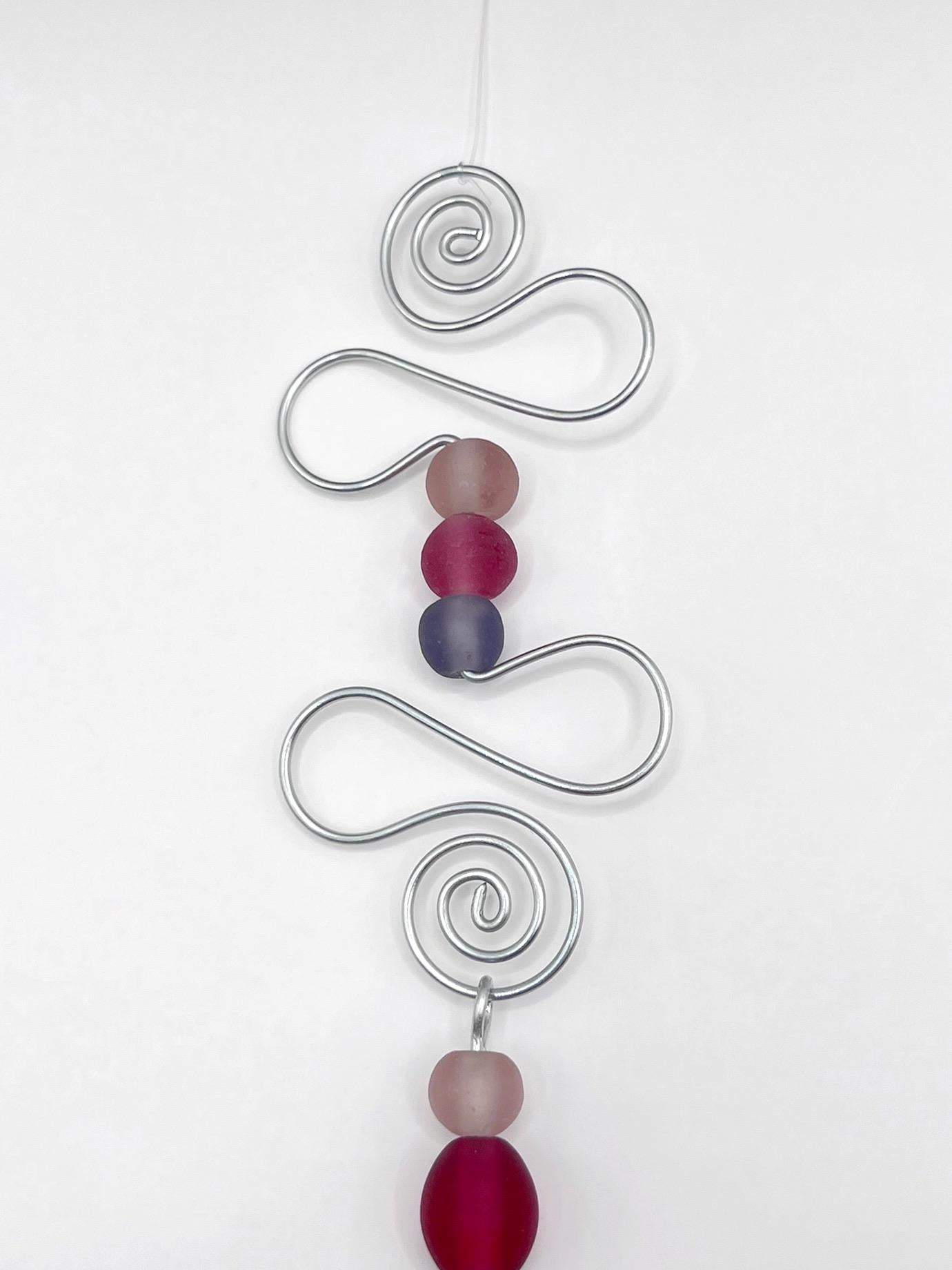 Close up of decorative ornament with blue fish, wire and colourful beads on a white background
