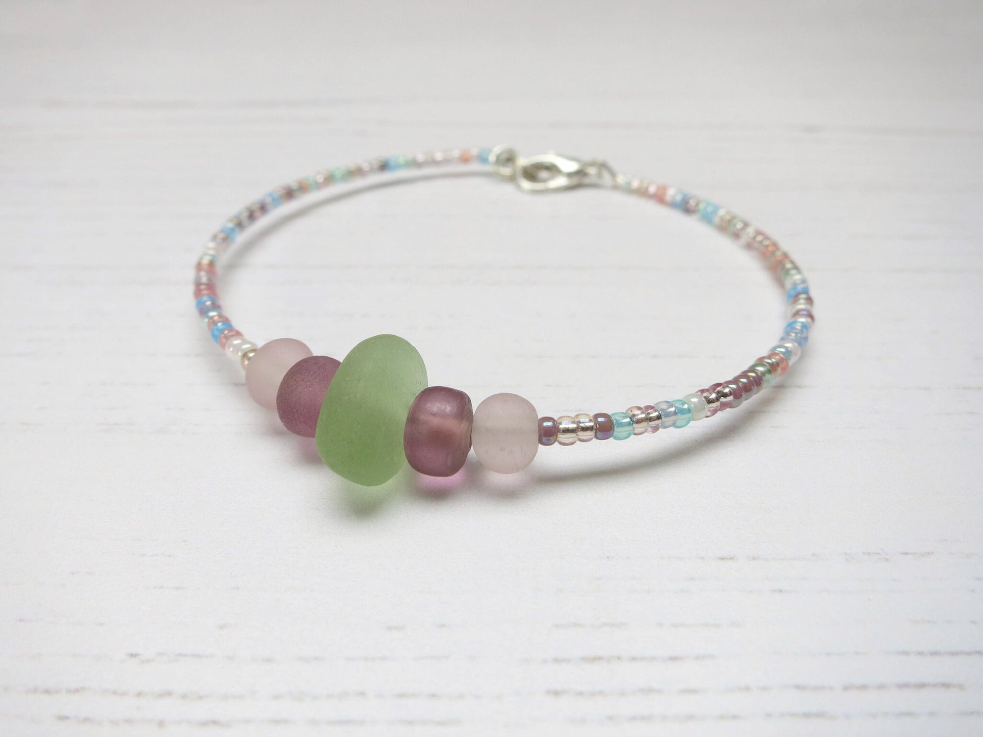 Pastel seed beaded bracelet with pale green sea glass laid on a pale background