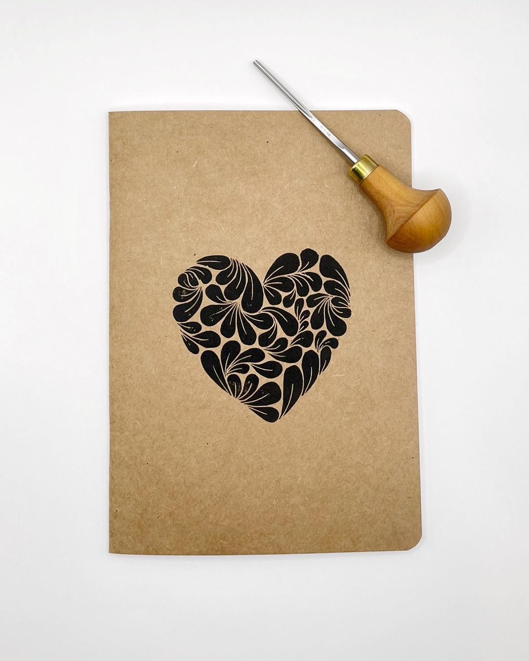 Kraft paper notebook with an original  black lino printed heart design. Photo includes the lino cutting tool used to make it.
