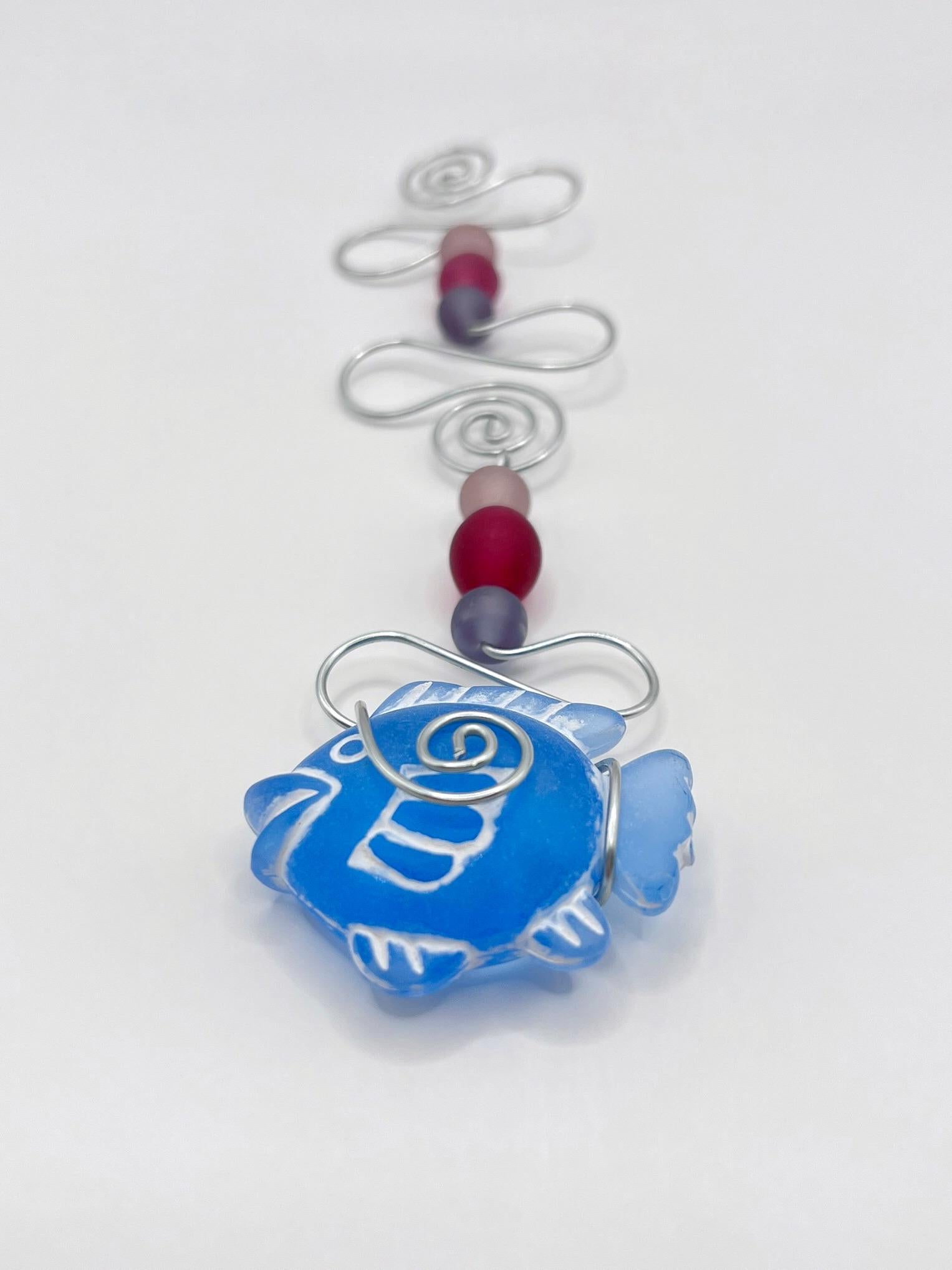 Decorative hanging mobile with blue fish, wire and colourful beads on a white background