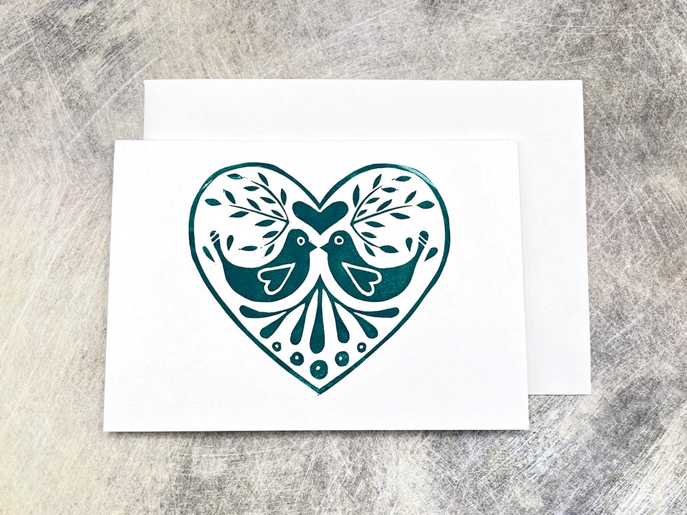 White card with a green heart design featuring two birds laid on a grey textured surface