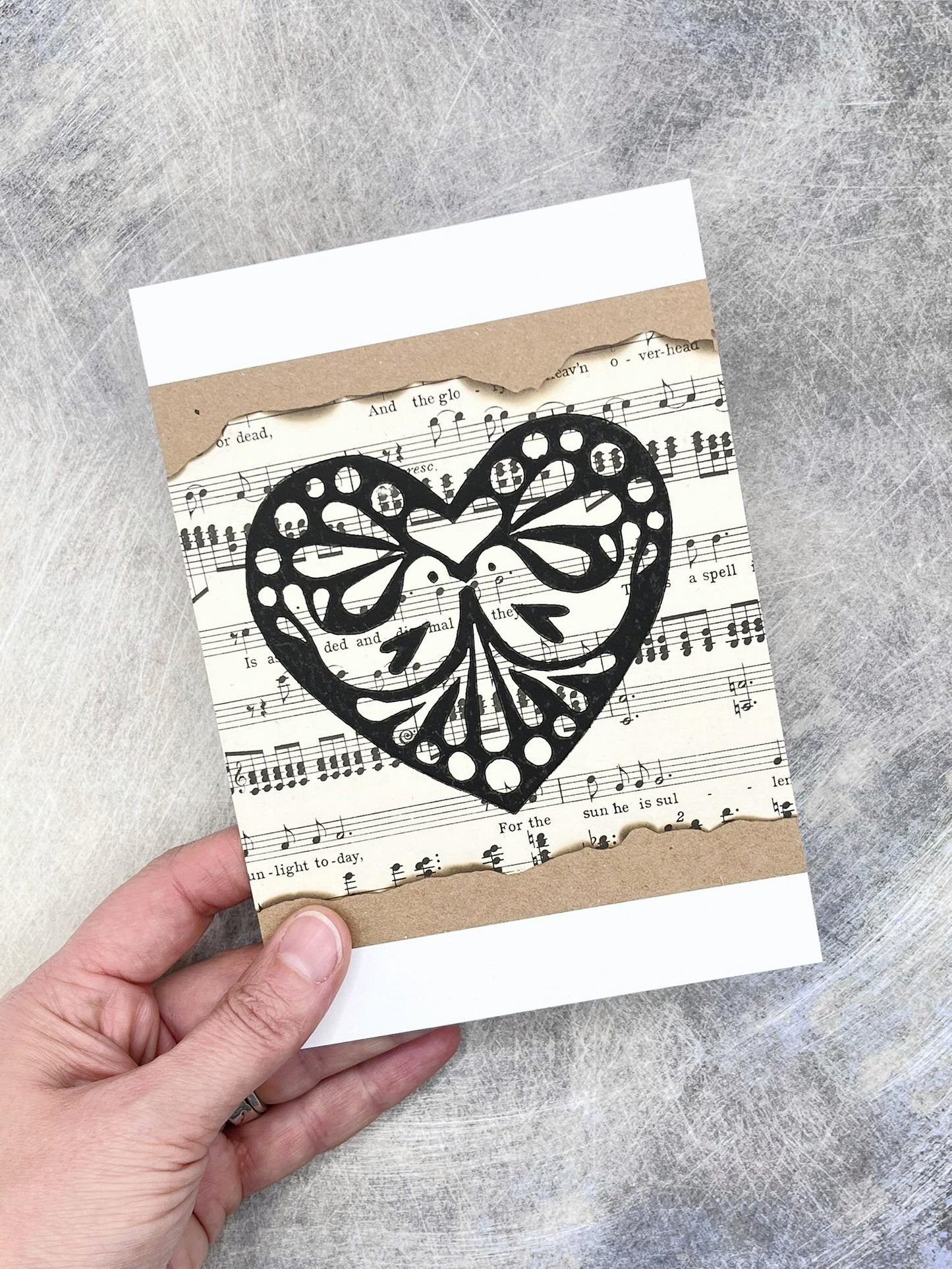 Hand holding a card with a black heart design on a sheet music background